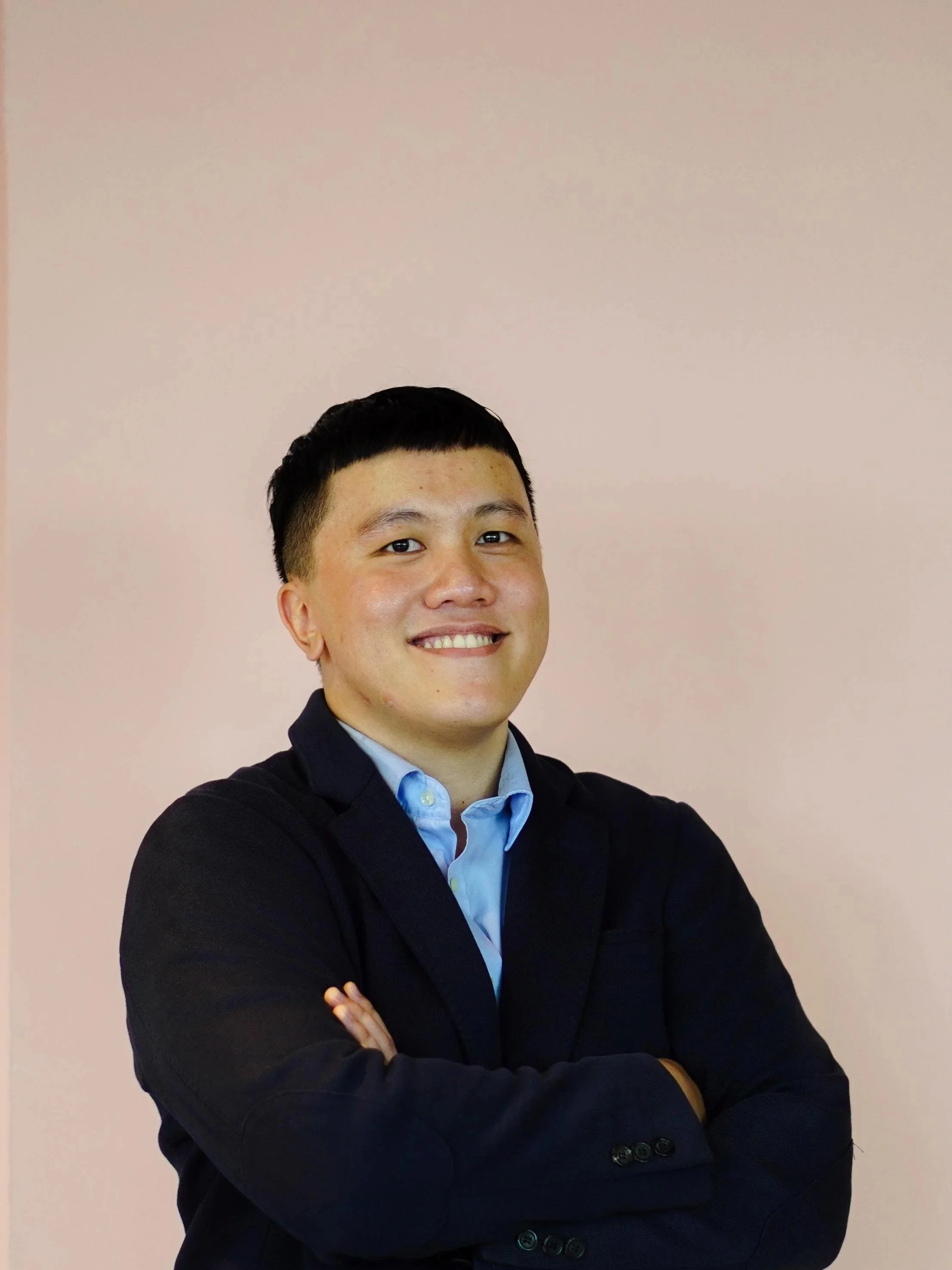 An Indonesian man smiling in front of a pink wall.