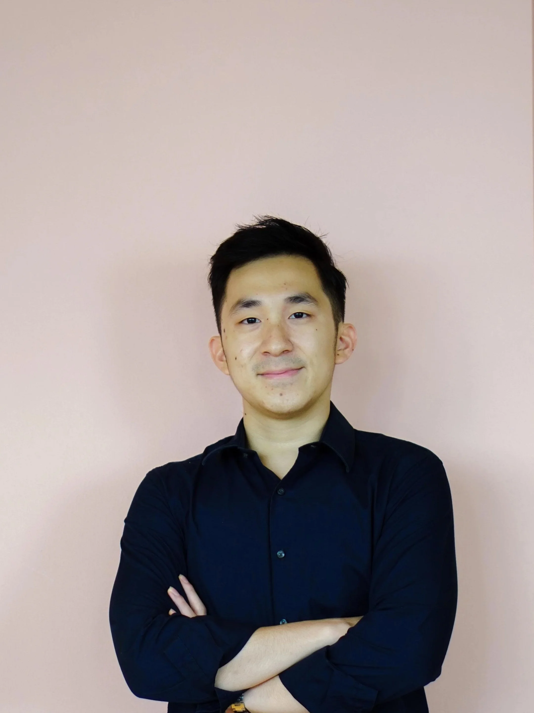 A Chinese-Indonesian man wearing a navy button-up posing in front of a pink wall.