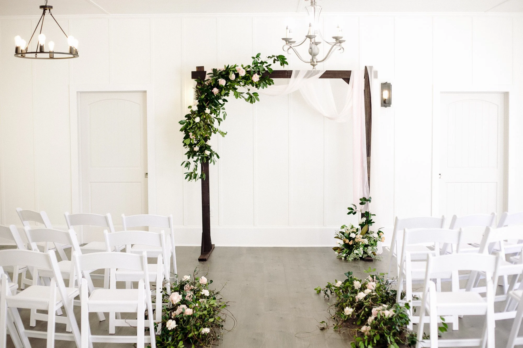 Wedding arch decorated with greenery and flowers, with chairs arranged for a ceremony in a bright, white room. Garden Wedding venue Atlanta Georgia The Wildflower 301