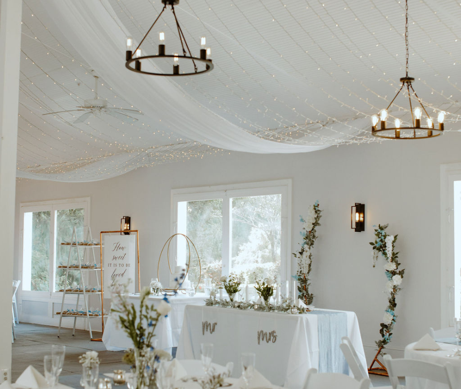 Elegant indoor wedding reception with white draped ceiling, fairy lights, chandeliers, and decorated tables with floral arrangements. Garden Wedding venue Atlanta Georgia The Wildflower 301