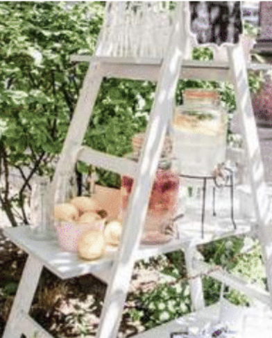 White wooden ladder decorated with pastel-colored eggs, pink polka-dot napkin, and small plants, set outdoors among green foliage. Garden Wedding venue Atlanta Georgia The Wildflower 301