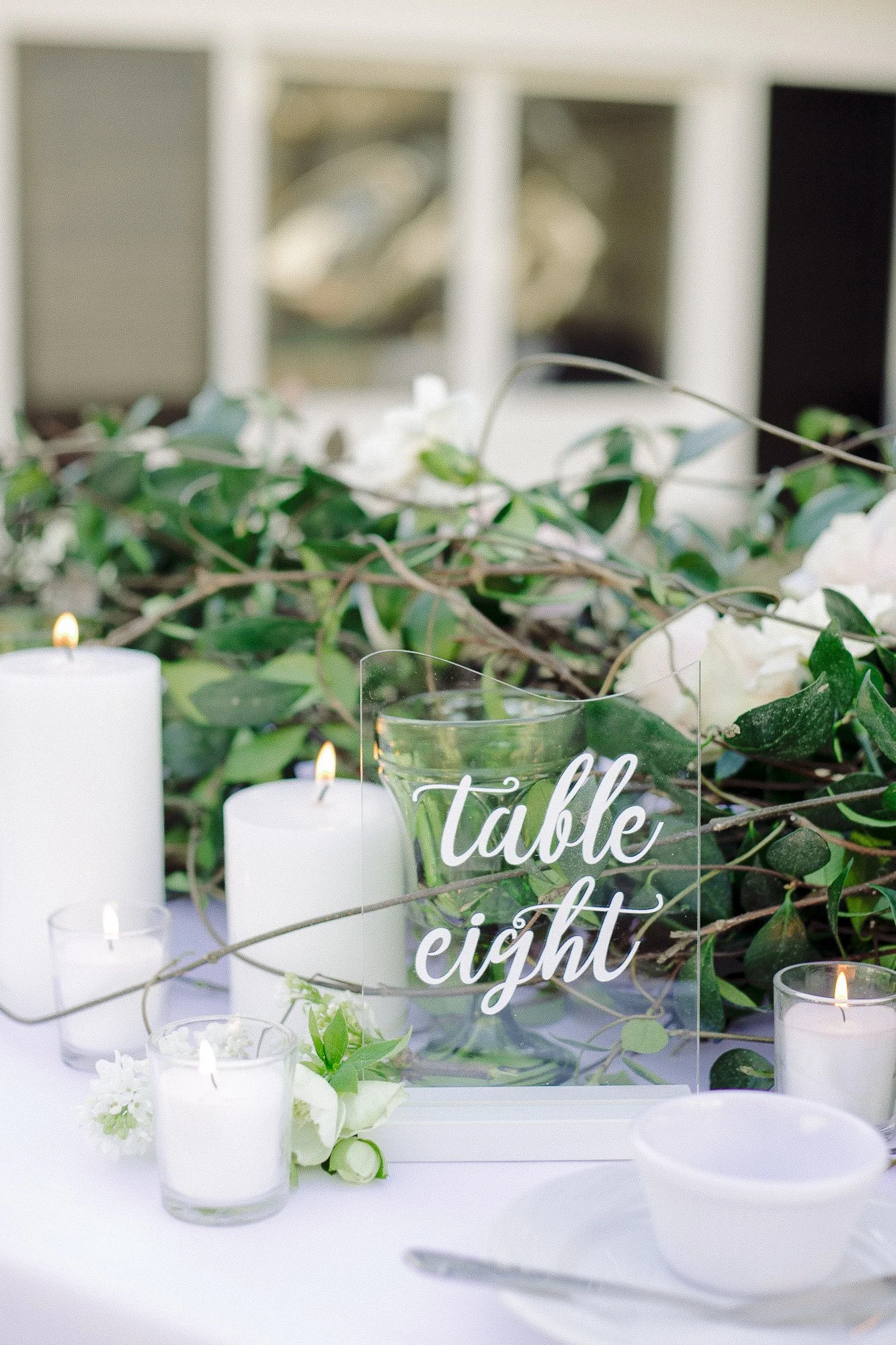 Wedding reception table decorated with white candles, white flowers, green foliage, and a glass sign that reads 'table eight'. Garden Wedding venue Atlanta Georgia The Wildflower 301