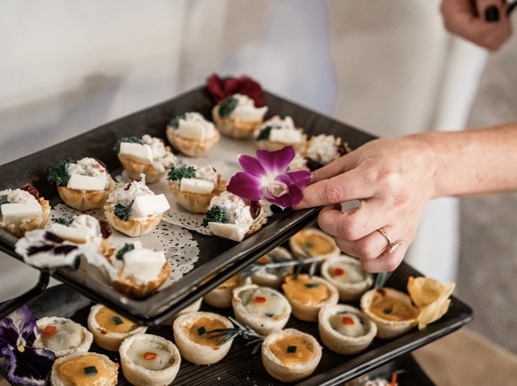 Hand arranging mini savory tarts with flowers on a tray at a catering or party setting. Garden Wedding venue Atlanta Georgia The Wildflower 301
