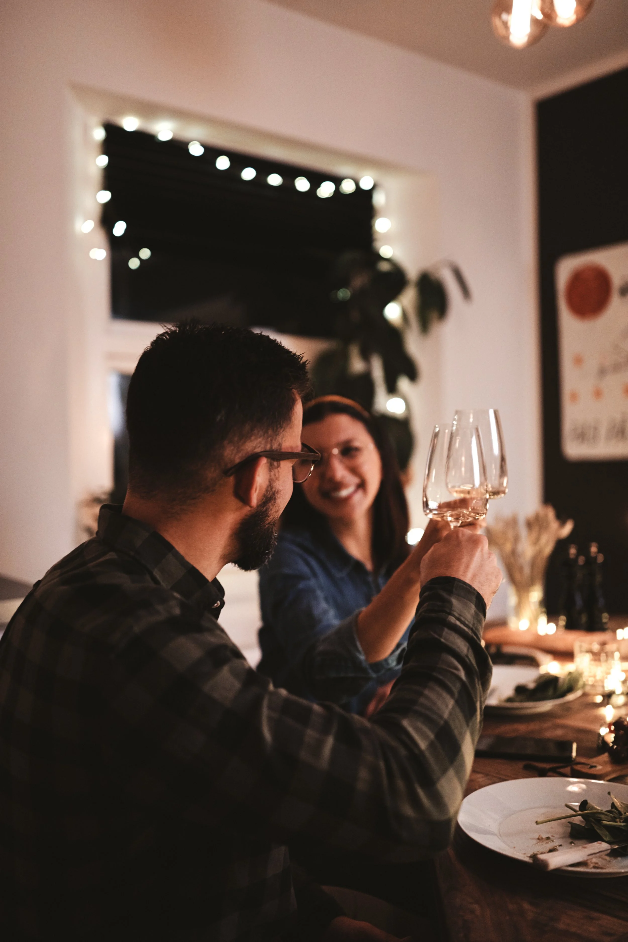 A man and woman clinking wine glasses at a dinner table during a cozy, warmly lit gathering. Garden Wedding venue Atlanta Georgia The Wildflower 301