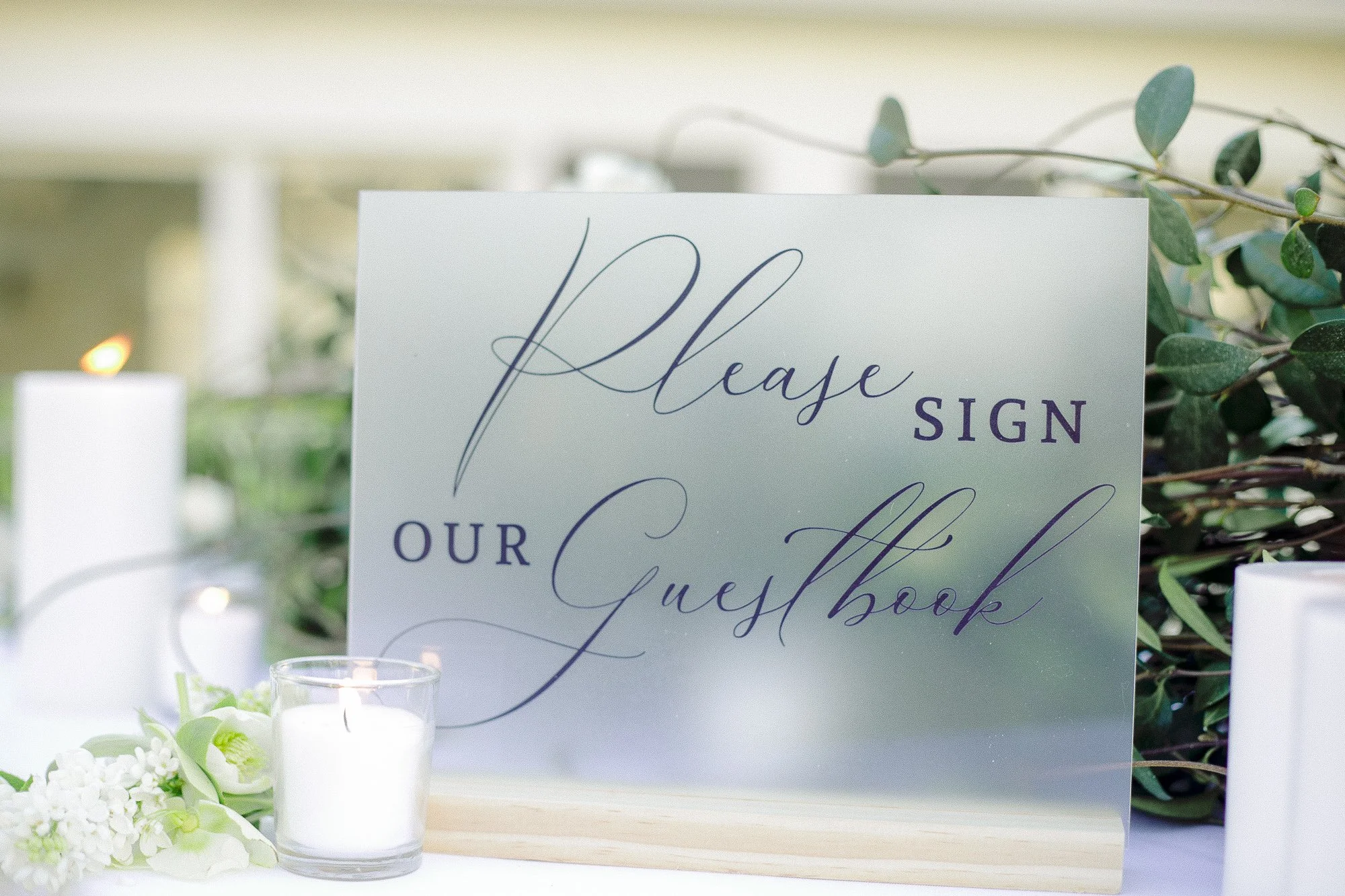 Wedding guest book sign with elegant script reading "Please sign our guestbook," surrounded by flowers and candles. Garden Wedding venue Atlanta Georgia The Wildflower 301