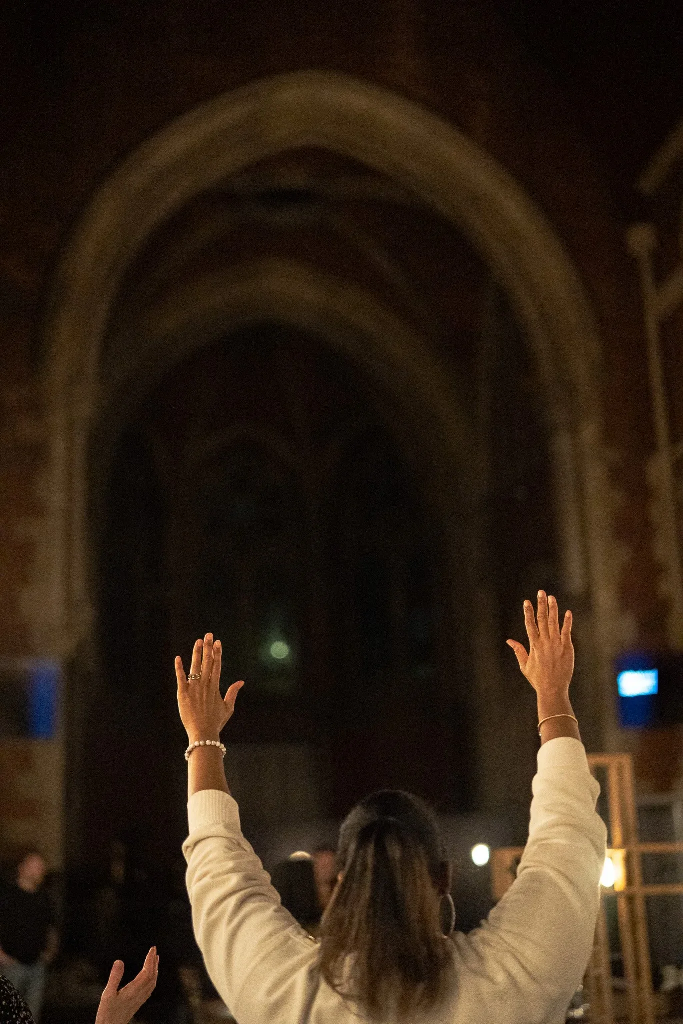 Woman raising both hands in worship inside a dimly lit church