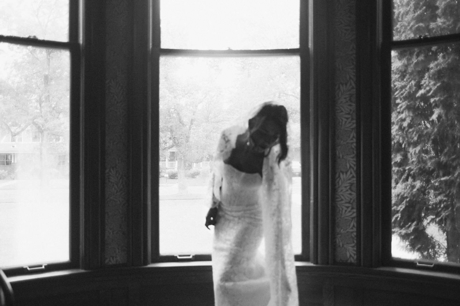 A woman in a white wedding dress with lace sleeves, standing in a doorway between two bookshelves.