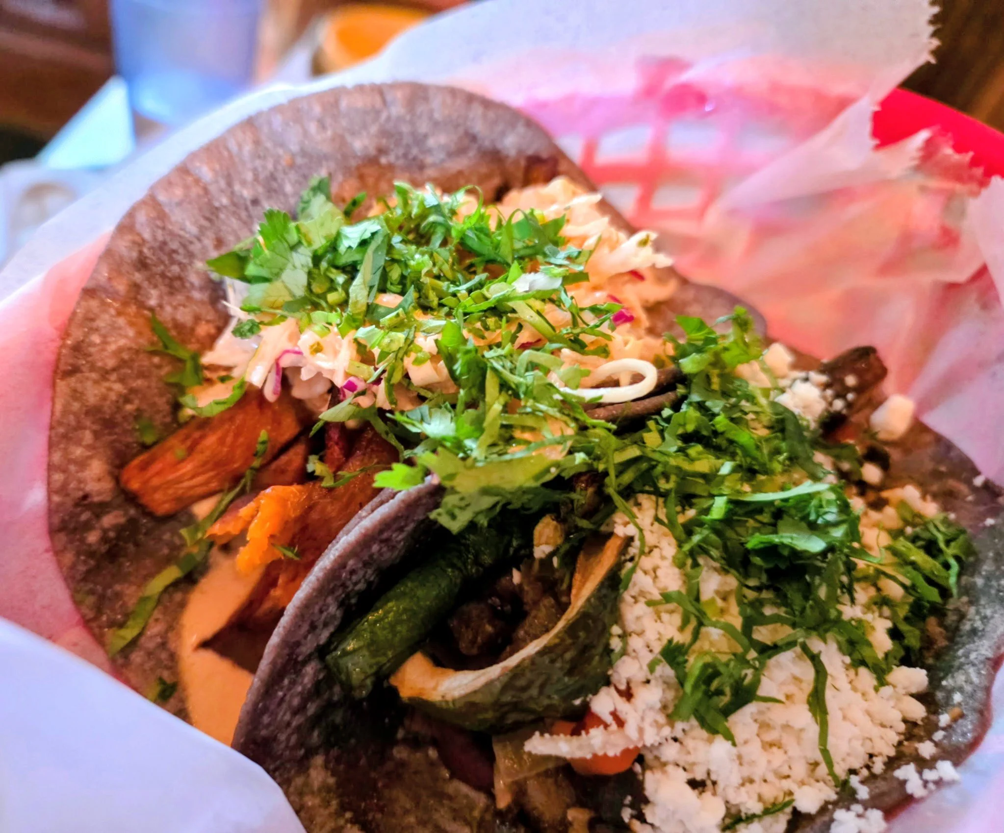 A close-up of a taco filled with chopped lettuce, shredded cheese, and grilled meat, wrapped in pink paper.