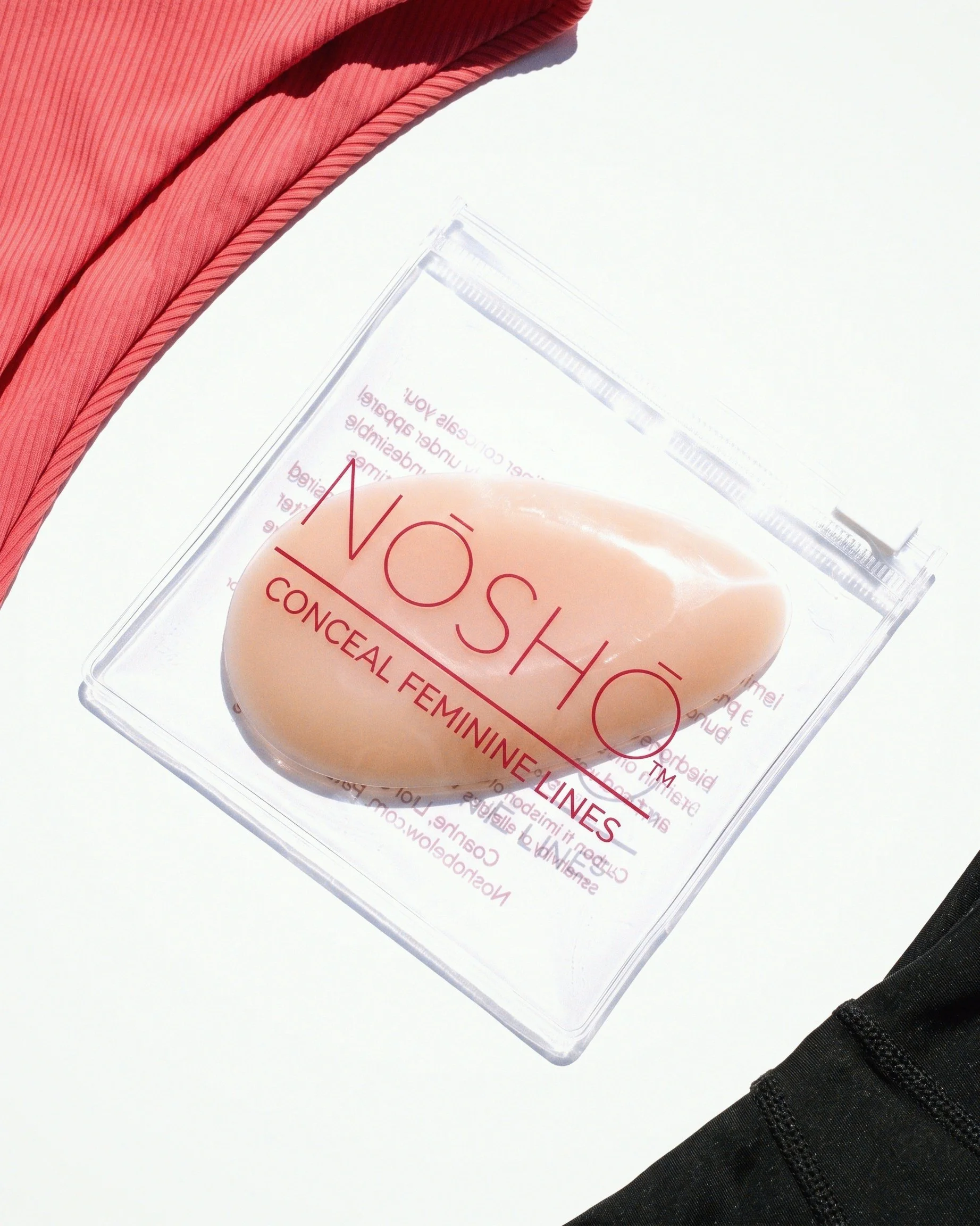 NŌSHŌ Below silicone insert in transparent branded pouch photographed with red and black fashion fabric