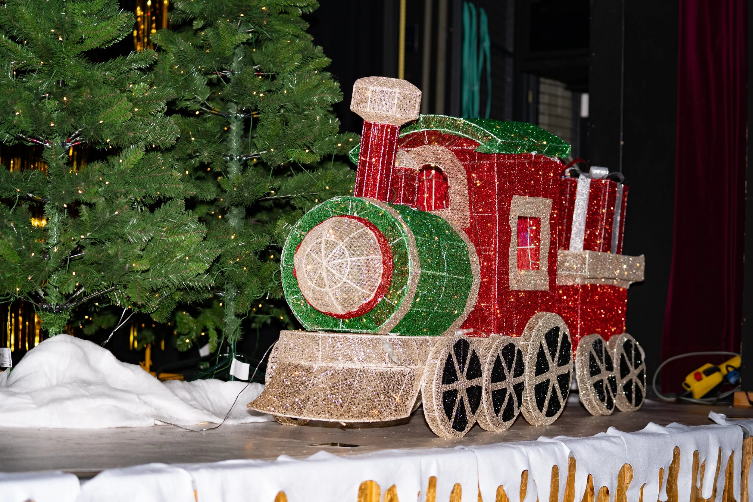 A glittery Christmas train decoration placed under a decorated Christmas tree with green and gold ornaments and lights.