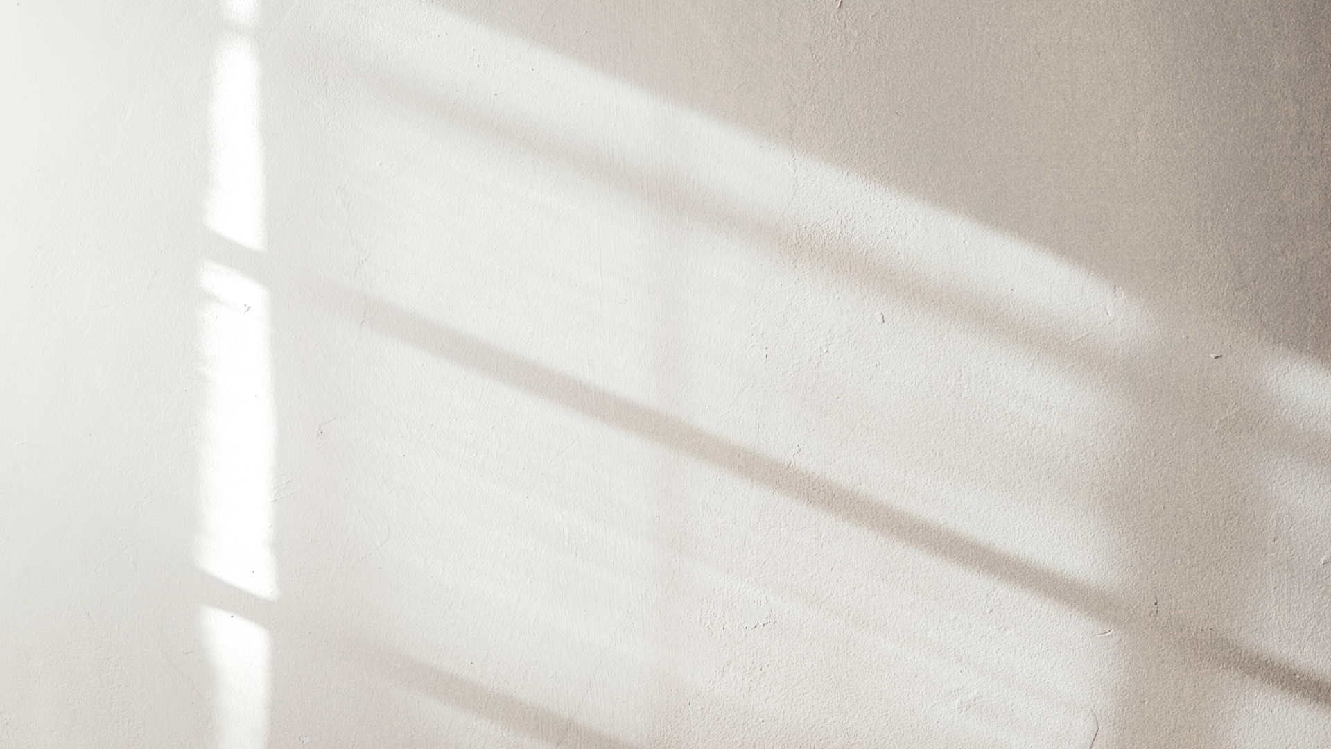 Sunlight streaming through a window casting shadows on a white wall.