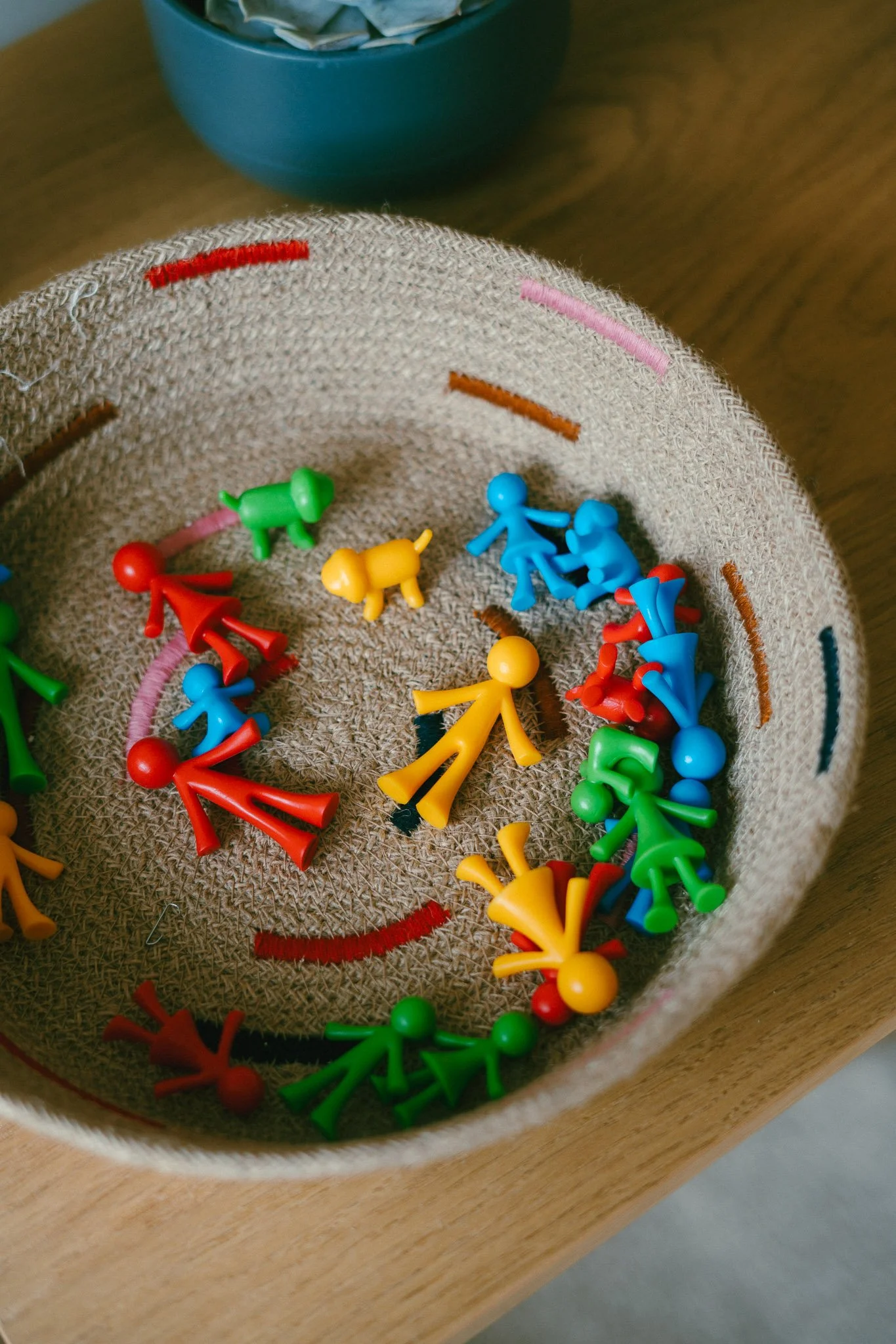 Colorful plastic figurines inside a fabric bowl on a wooden surface, with a blue container in the background.