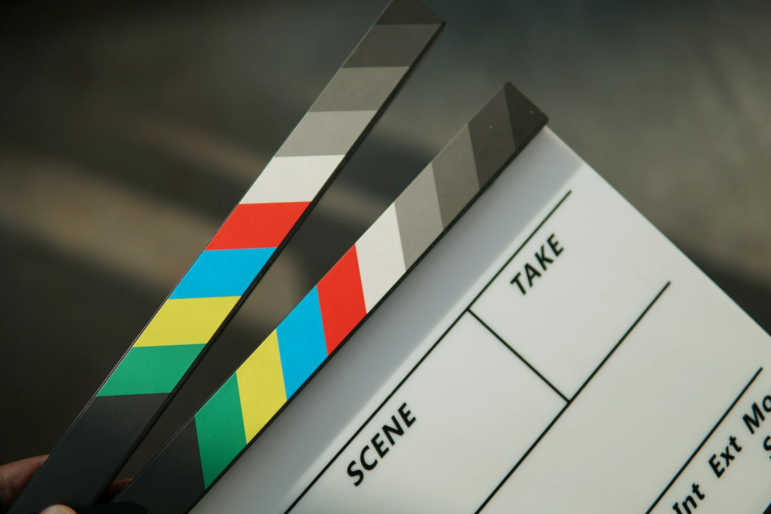 Close-up of a film clapboard with colorful stripes on the edge and partially visible text for scene, take, and other film production information.