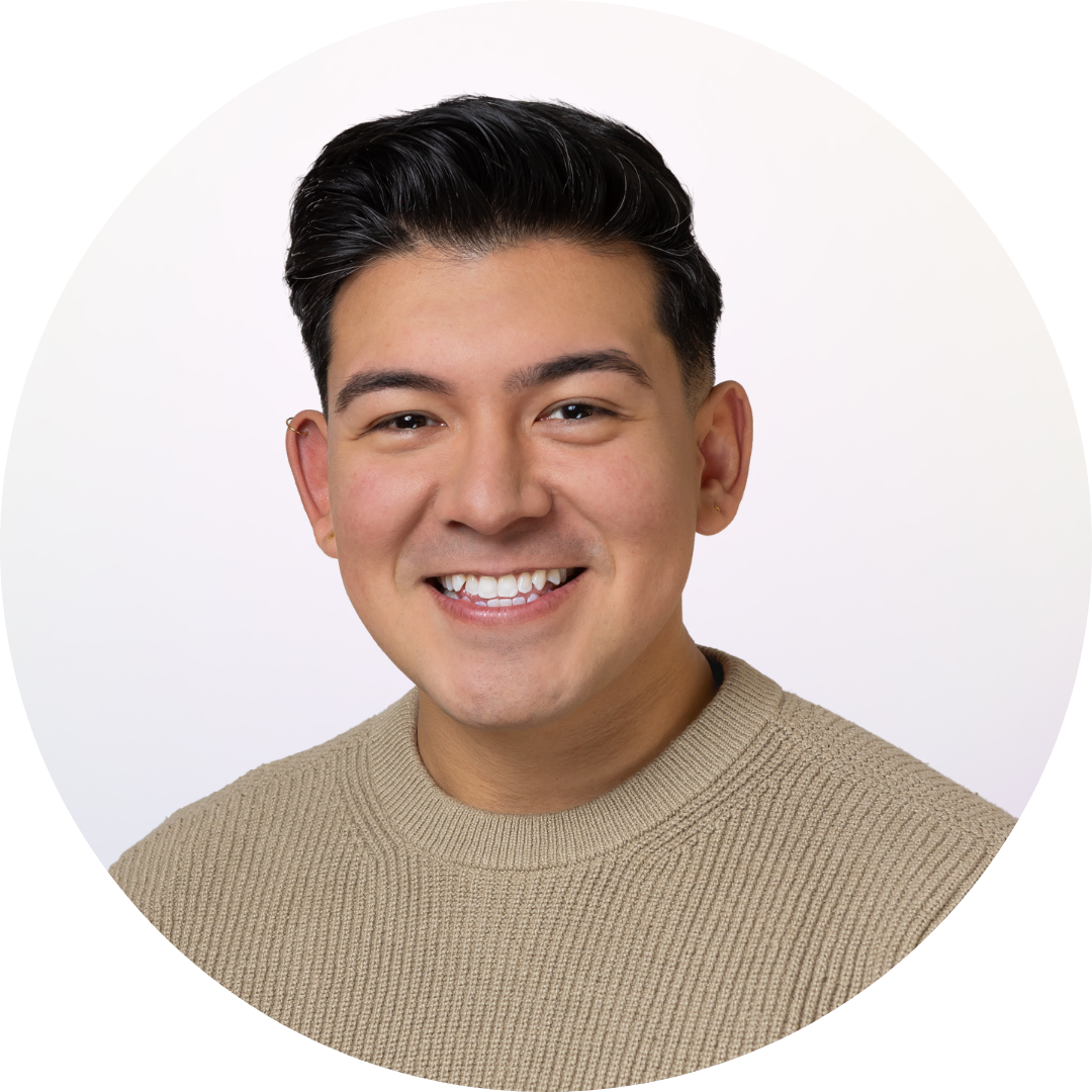 A young man with dark hair smiling, wearing a beige knit sweater, against a white background.