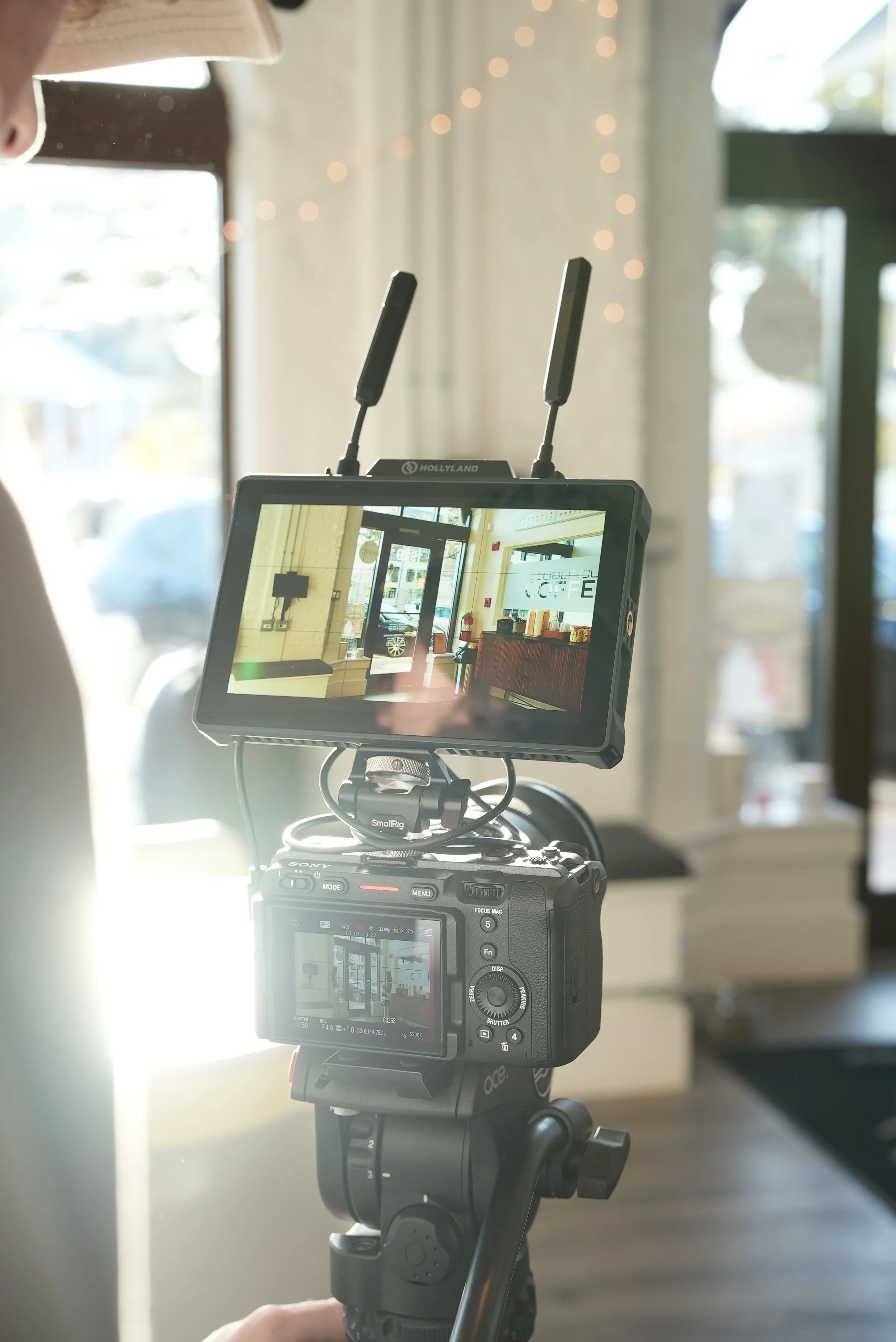 A camera on a tripod recording an indoor scene of a cafe entrance with large windows, a counter, and chairs inside.