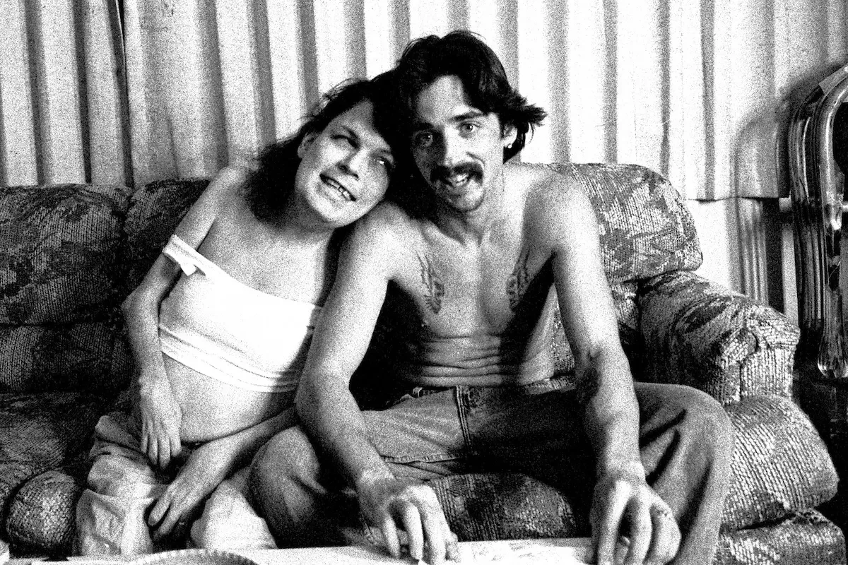 Black and white photo of a man and woman sitting on a patterned couch, smiling and showing affection.