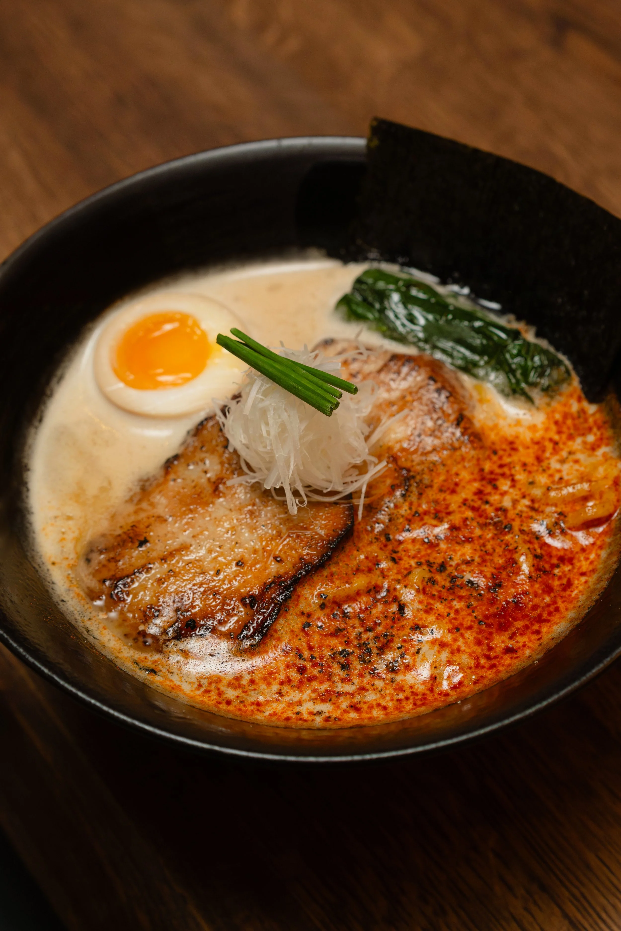 Bowl of Tonkotsu ramen with a soft-boiled egg, binchotan-grilled pork, seaweed, spinach, shredded white onion, and seasoning in a creamy broth