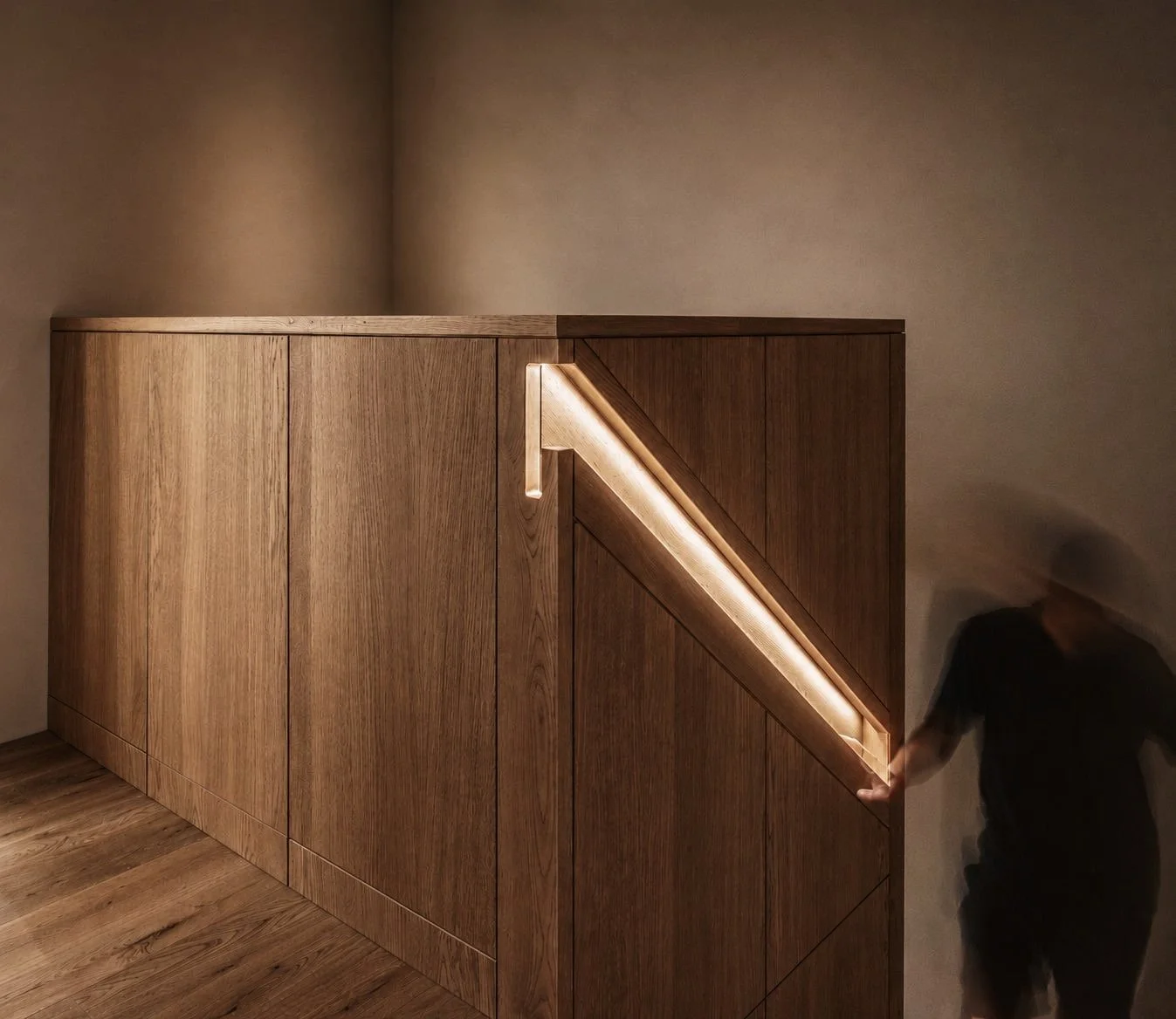 Trap van hout met ingebouwde LED-verlichting langs de rand, in een kamer met houten vloer en beige muur. Een persoon staat links van de kast, maar is blurry en moeilijk te herkennen.