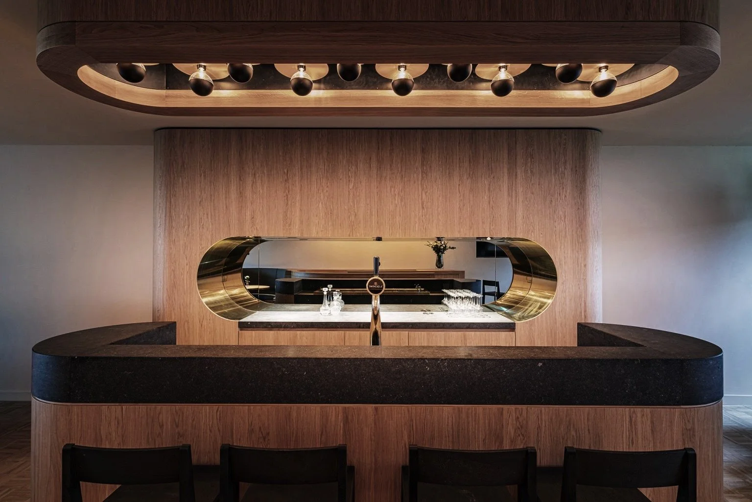 Binnenkijking van een moderne bar met houten en zwarte elementen, een grote spiegel, en barkrukken in een skybox in PSV Stadion.