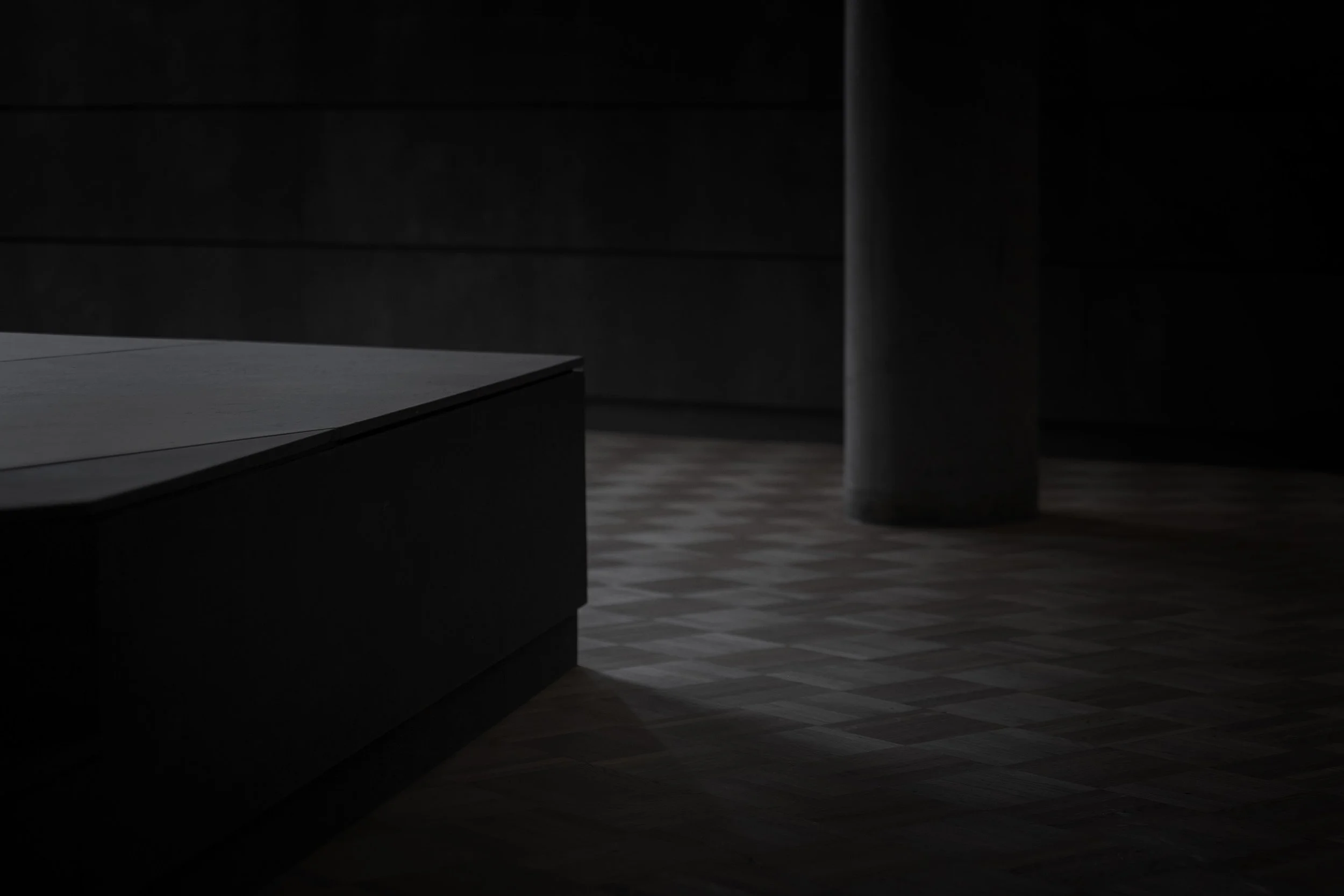 Donkere, minimalistische kamer met een tafel en een vaas, weinig licht.