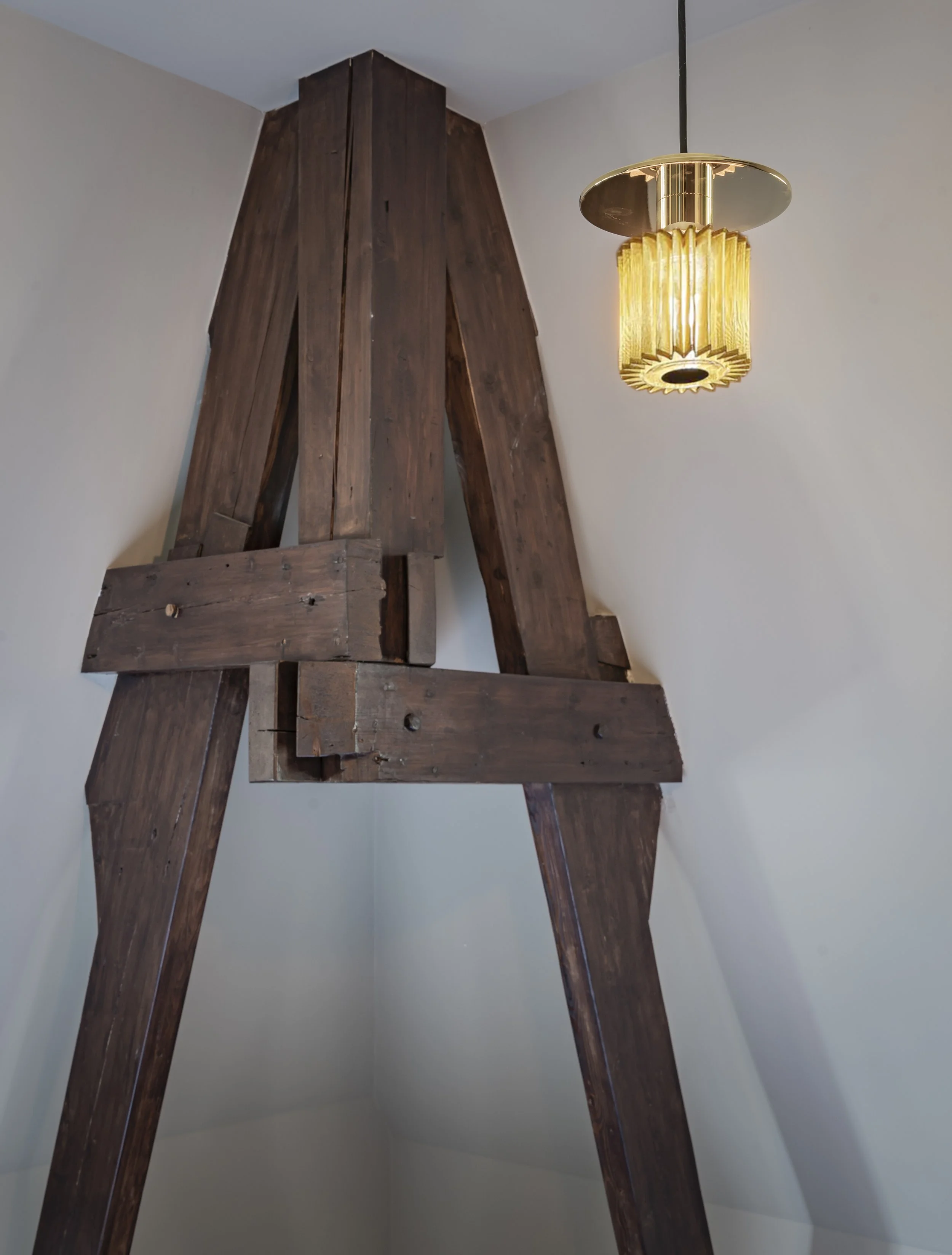 Een houten constructie in een kamer van een Bed and Breakfast in Venlo met witte muren en een plafond, verlicht door een goudkleurige design hanglamp van DCW Editions.
