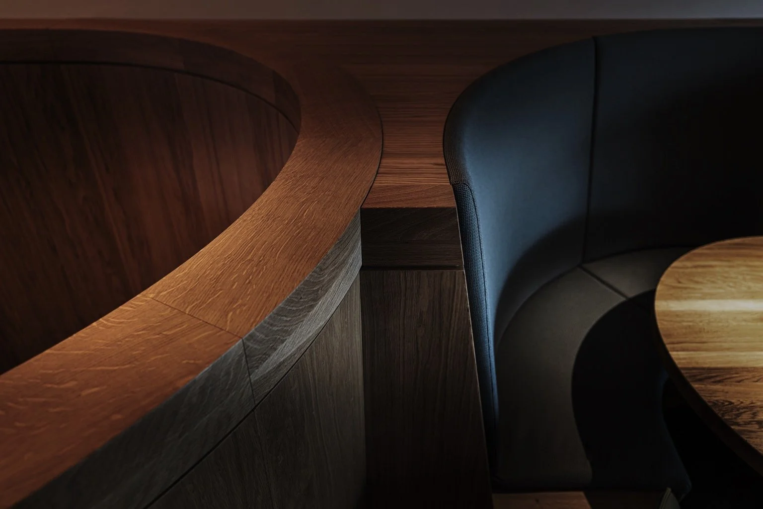 Close-up van een ontworpen maatwerk element zoals een ronde houten tafel en een gebogen zitbank in een modern interieur van  een Skybox in PSV stadion Eindhoven.
