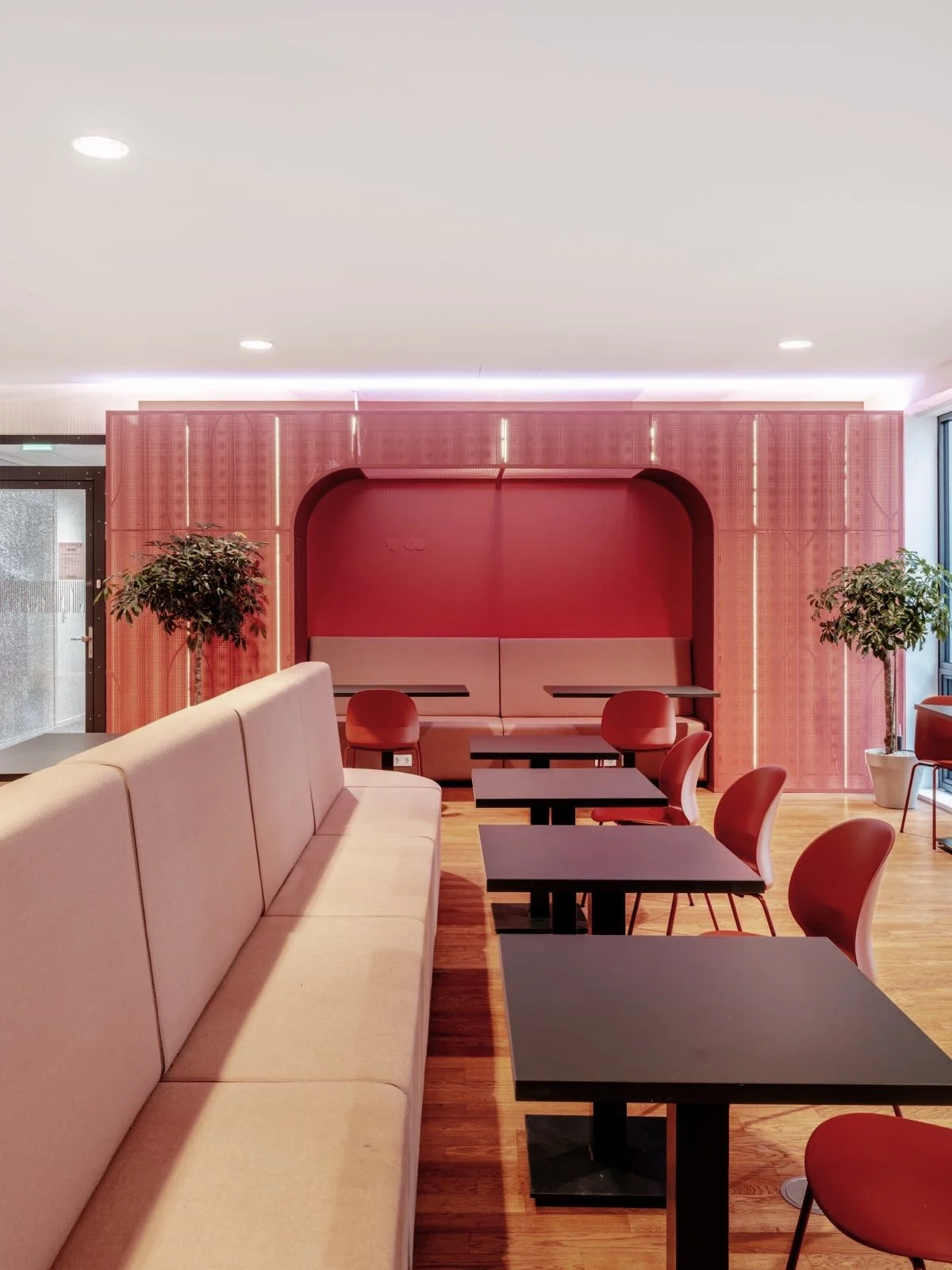 Modern interieur in een café of restaurant met beige banken, rode stoelen, en planten, muurbekleding in rood en roze tinten.