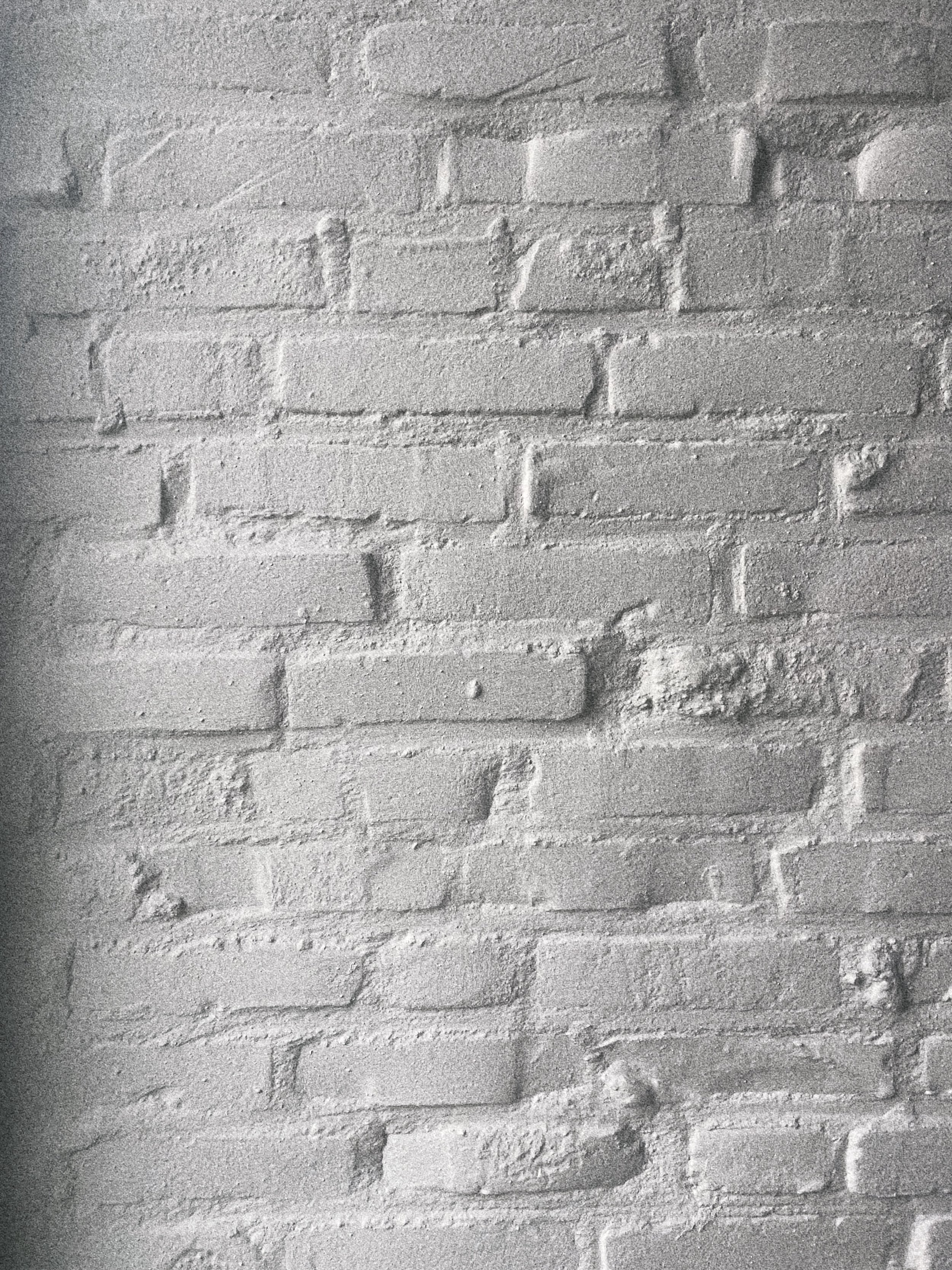 Lichtgrijze bakstenen muur met een ruwe textuur.