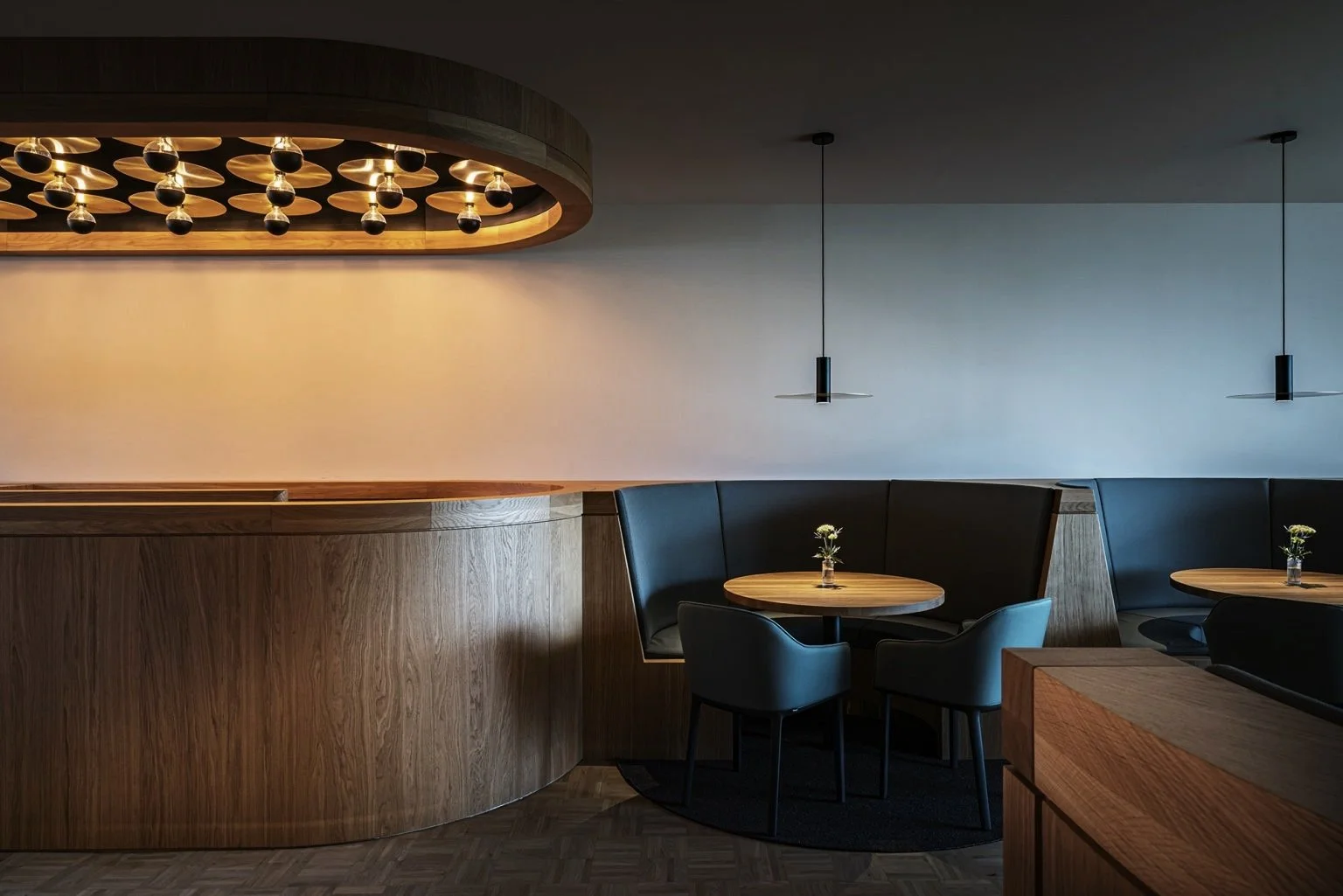 Modern rustige restaurant in een Skybox in Eindhoven bij PSV met maatwerk ronde houten tafels, stoelen, houten decor en sfeervol speciaal ontworpen verlichting.