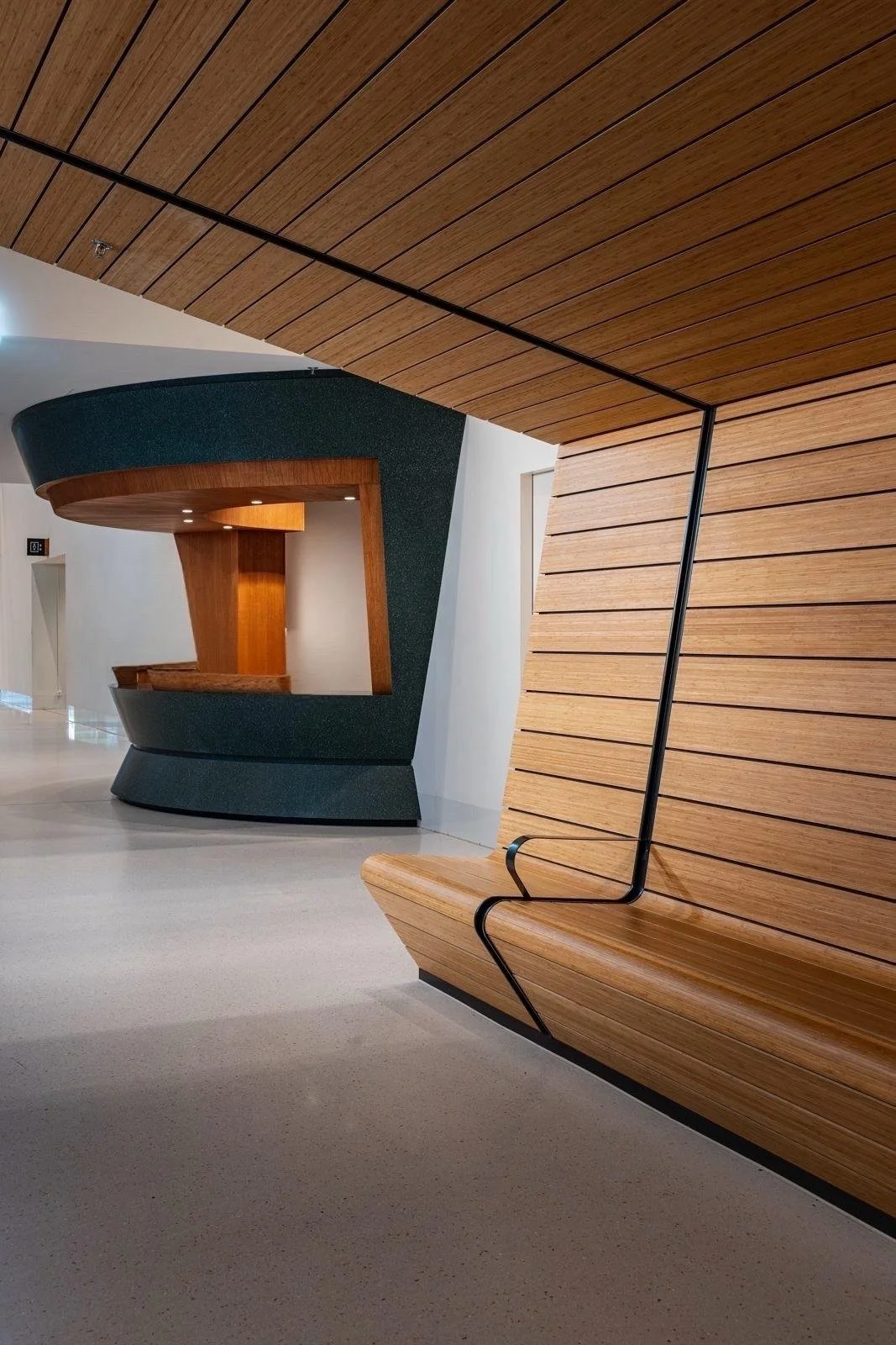 Interieur van een modern gebouw met houten plafond en wanden, een bank met een opvallende zwarte metalen armleuning, en een decoratief,Boekenkast of wand met een grote open ruimte.