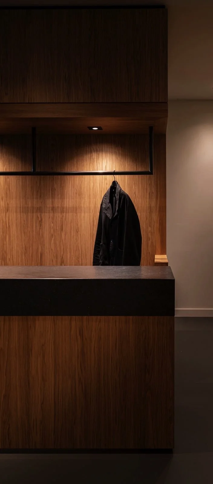 Houten balie met een zwarte jas aan een hanger, in een moderne, minimalistische ruimte met zachte verlichting.