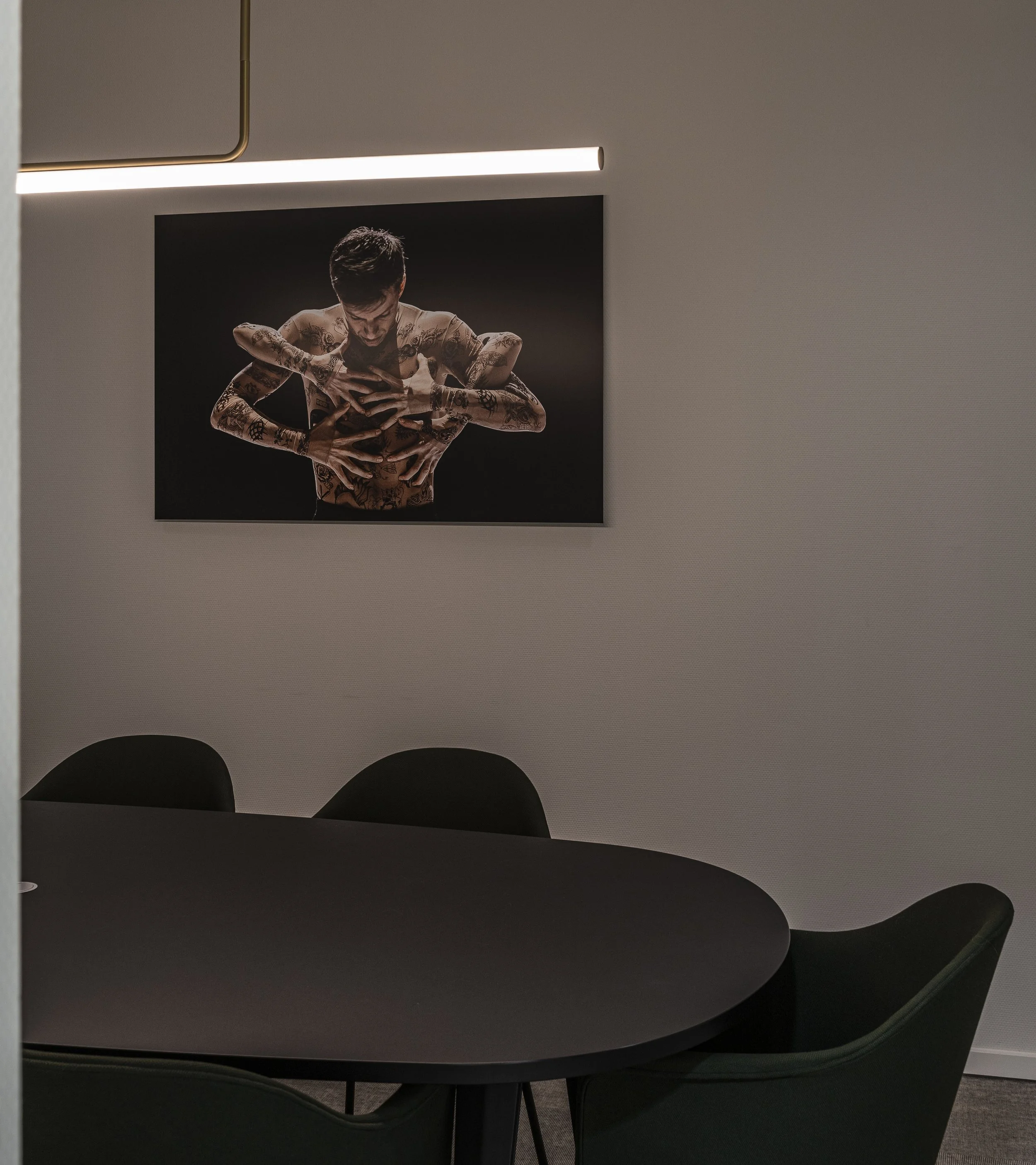 Foto van een vergadertafel en stoelen in een kantoorruimte met een foto van een tatoeëerde man op de muur.