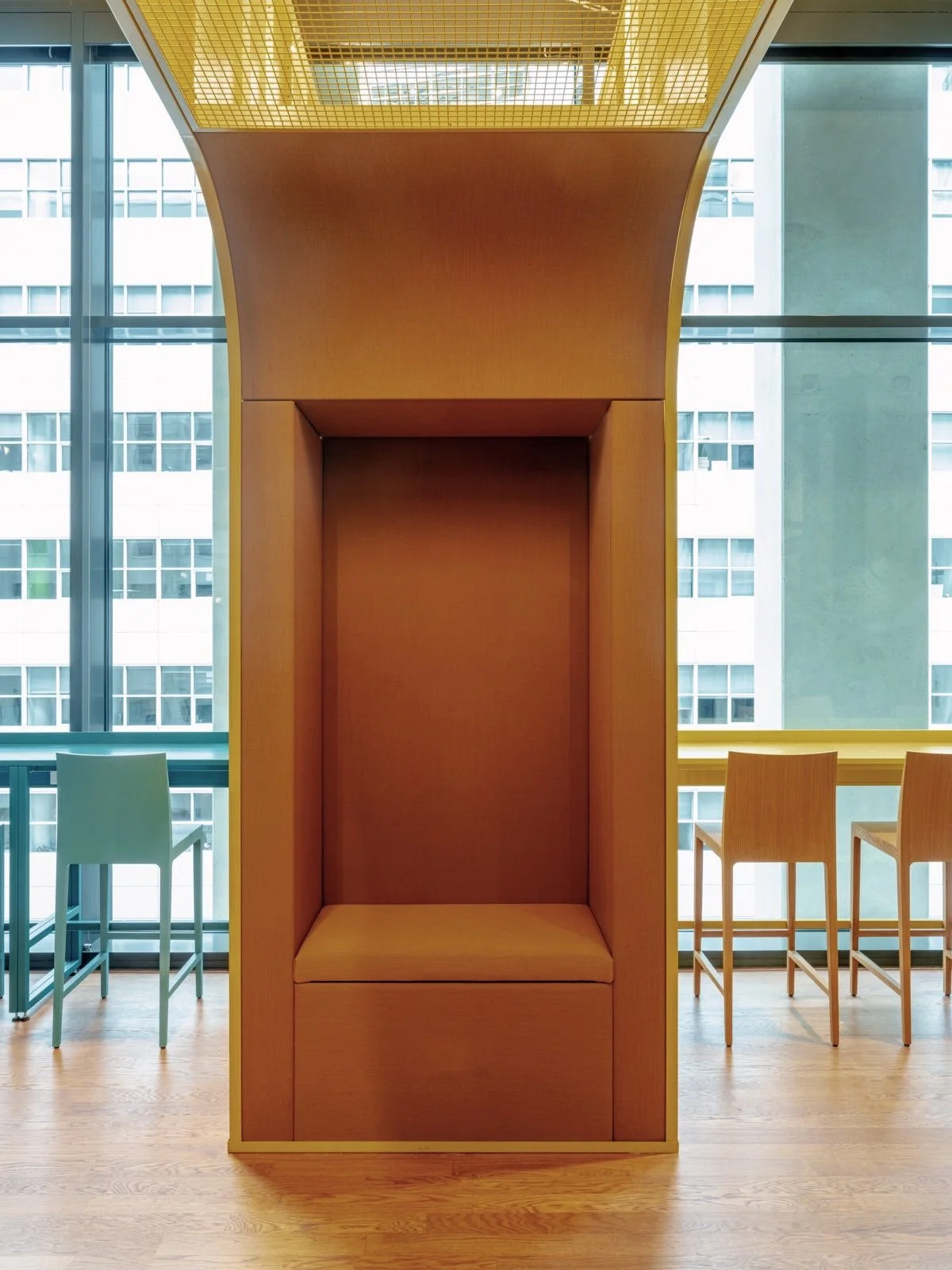 Leeg houten zitmeubel in een moderne binnenruimte met grote ramen en uitzicht op andere gebouwen.