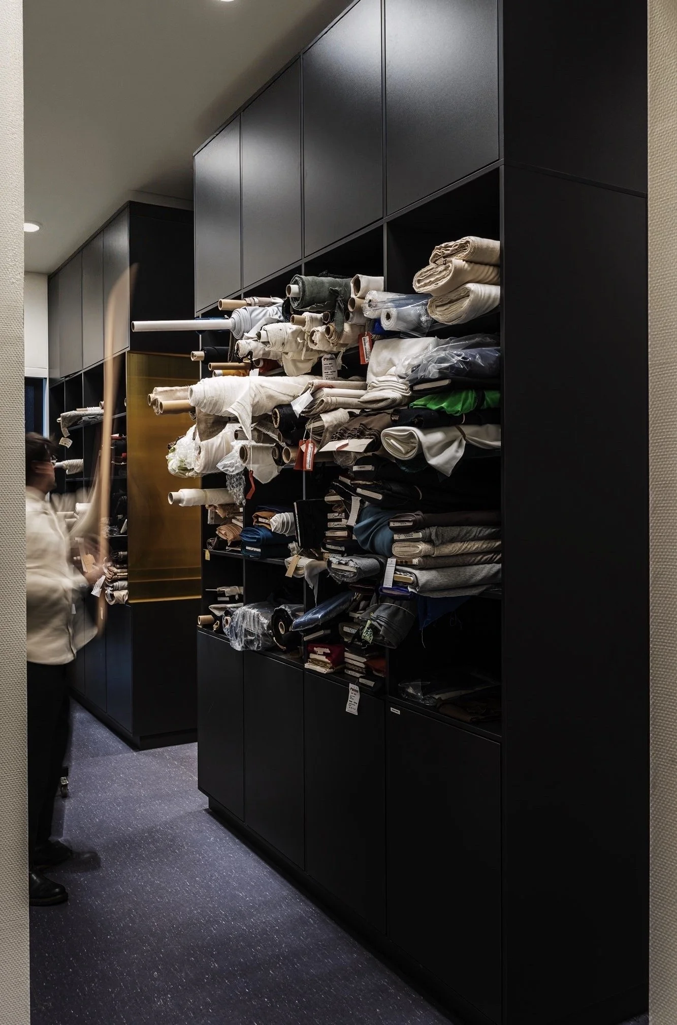 Een zwart metalen kast gevuld met verschillende stoffen en textielrollen, gevestigd in een winkel of kleedkamersituatie.