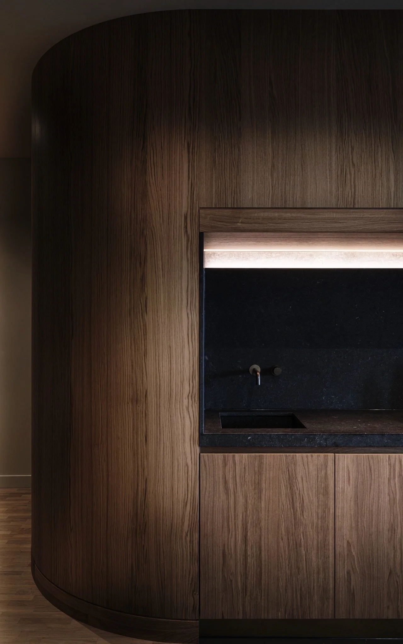 Detail van een modern houten keukenkast met een zwarte spoelbak en een kranen, in een minimalistisch keukenontwerp.