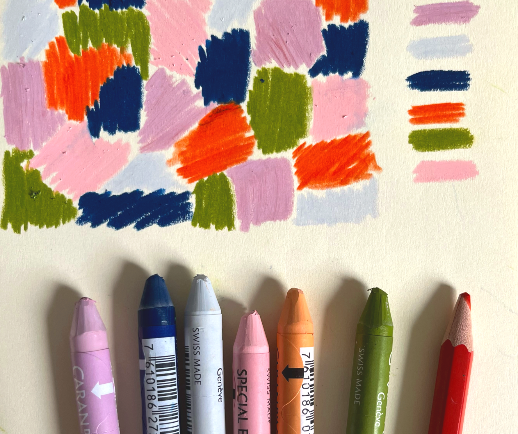Colorful markers arranged on a surface with a small abstract watercolor painting above them. The painting features pink, orange, green, blue, purple, and white brush strokes.