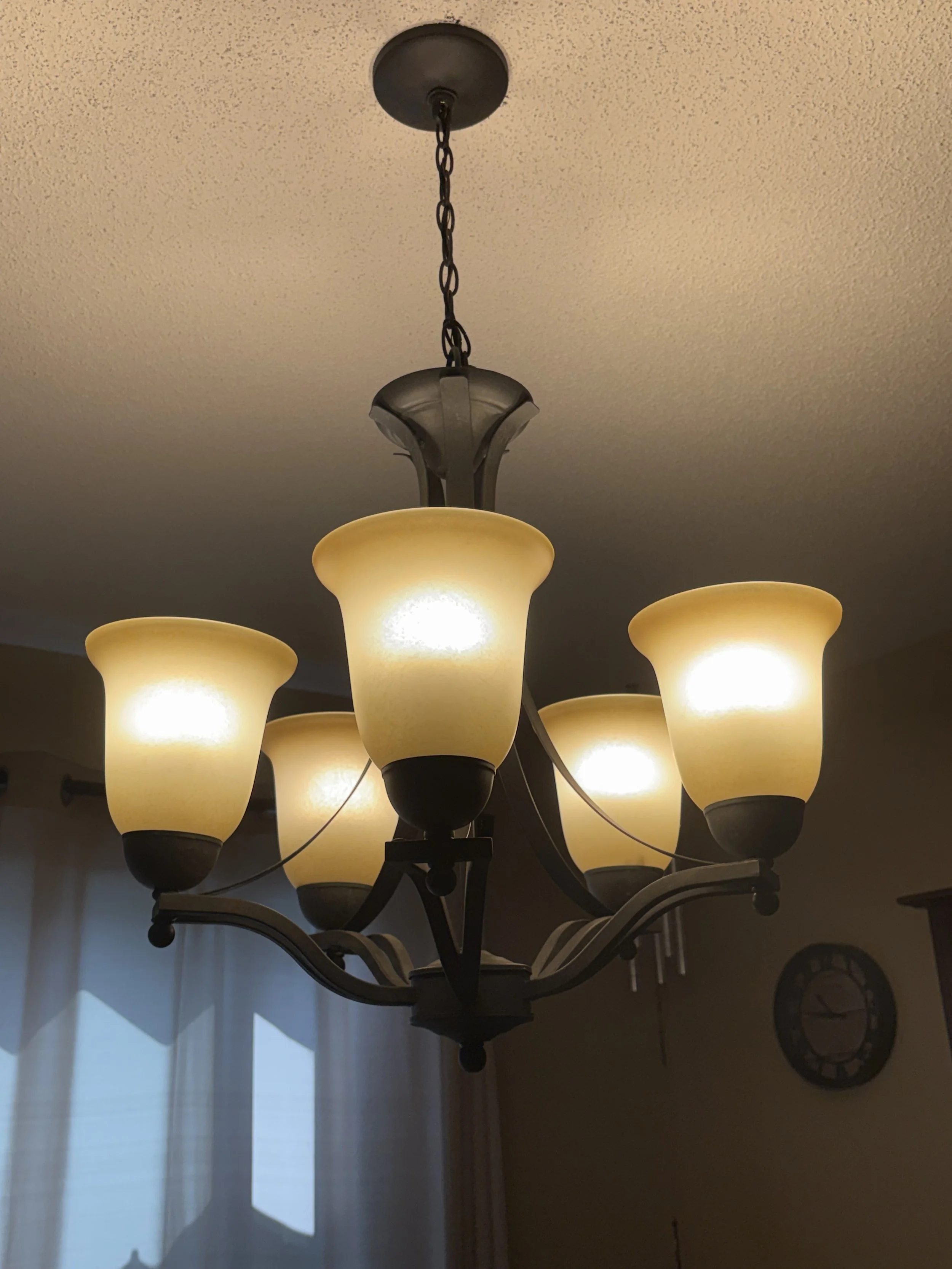 A chandelier with multiple cream-colored glass lampshades hanging from a chain attached to a ceiling.
