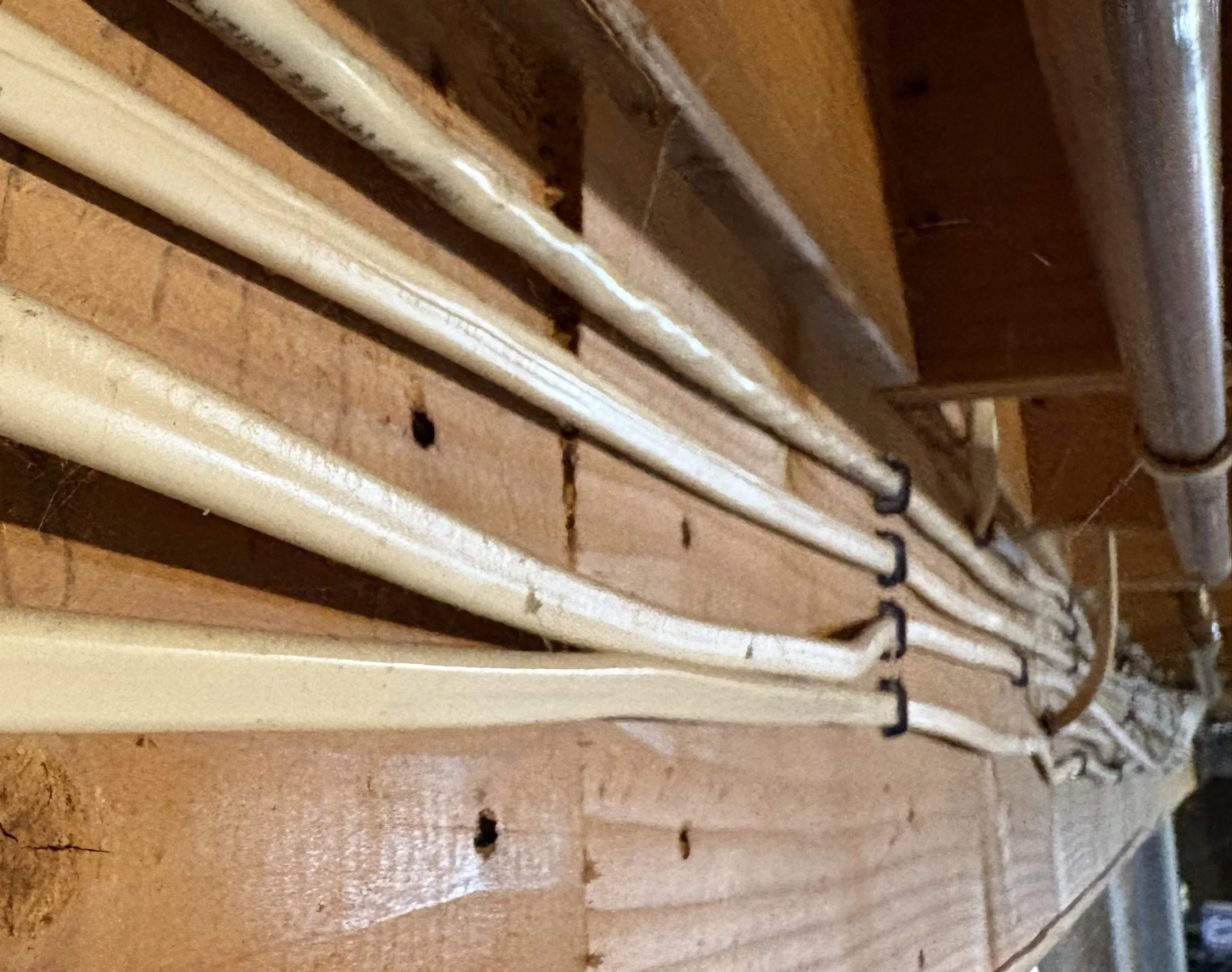 Close-up of white pipes running along a wooden surface with some exposed nails and small holes.
