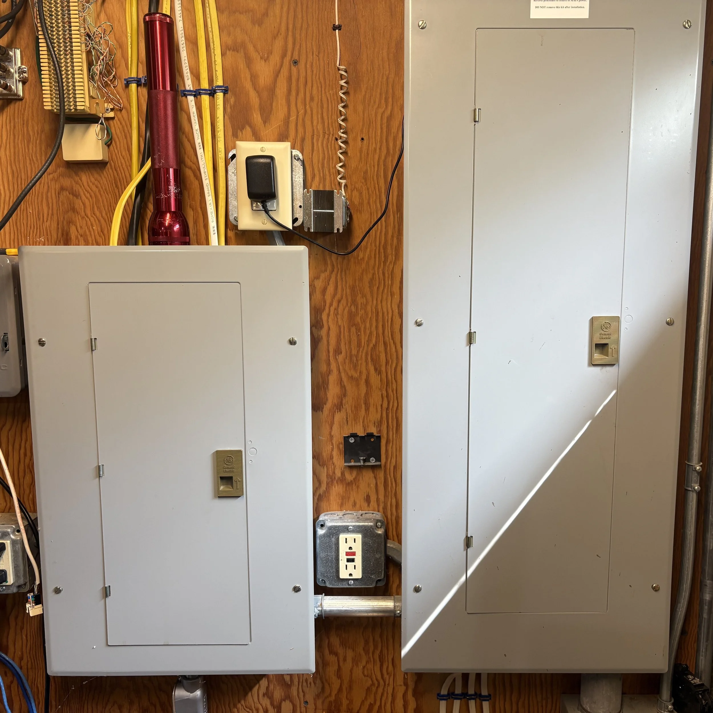 Electrical and electronic components mounted on a wooden wall, including power outlets, circuit breakers, and wiring.