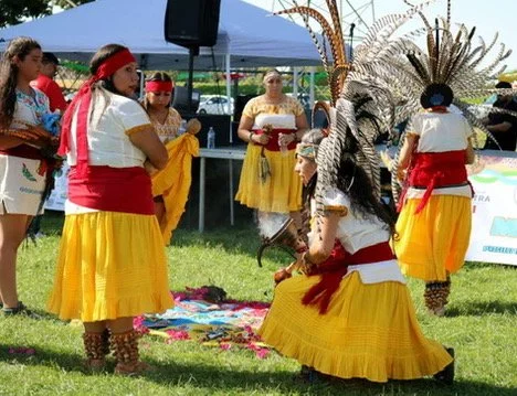 Indigenous dancers in colorful traditional attire performing at an outdoor cultural event.