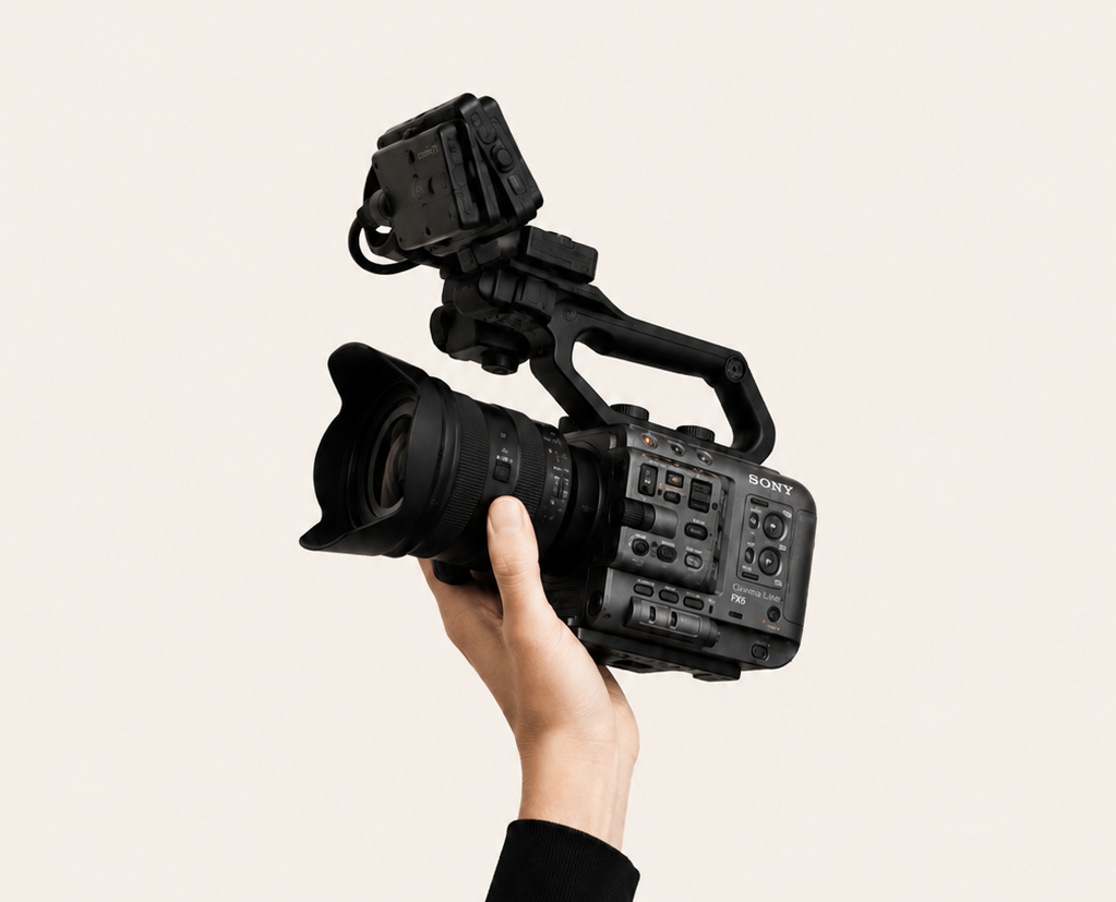 A person holding a professional Sony video camera with a large lens and accessories against a neutral background.