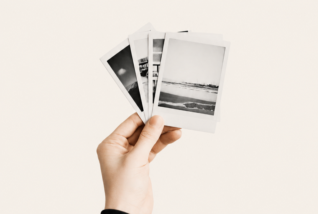 Hand holding five black-and-white instant photographs against a plain light background.