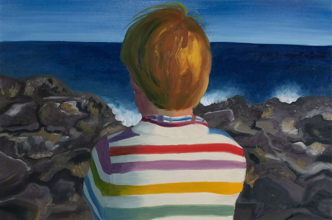 Child in rainbow stripe sweater gazes out over crashing ocean waves