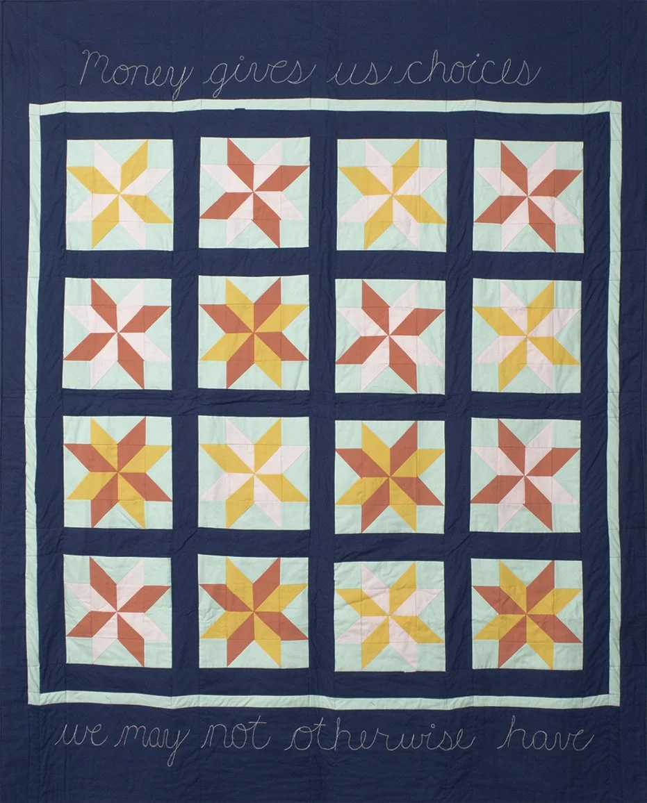 Blue quilt with gridded star design in yellow, orange, and pink, with the blue embroidered words, "Money gives us choices we may not otherwise have"