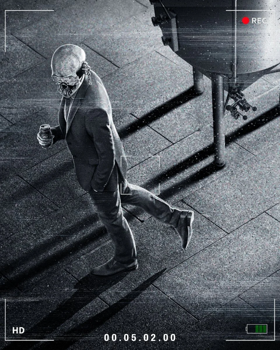 A black and white photo of a person in a suit and skull mask, walking on a tiled sidewalk while holding a drink. The photo has a camera viewfinder overlay with a red recording indicator and a battery icon.