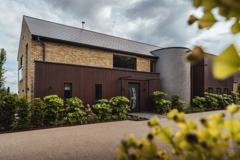 Modern two-story house with brick and wood exterior, landscaped front yard, and cloudy sky