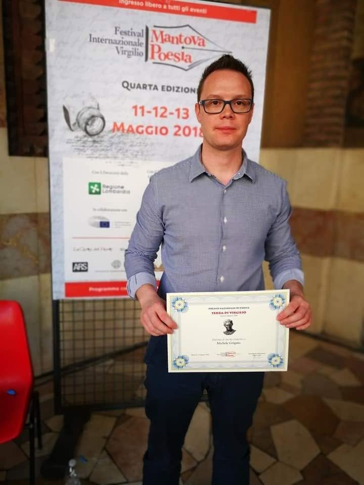 Uomo che tiene un certificato davanti a un poster del Festival Internazionale Virgilio a Mantova, che si tiene dal 11 al 13 maggio 2018.