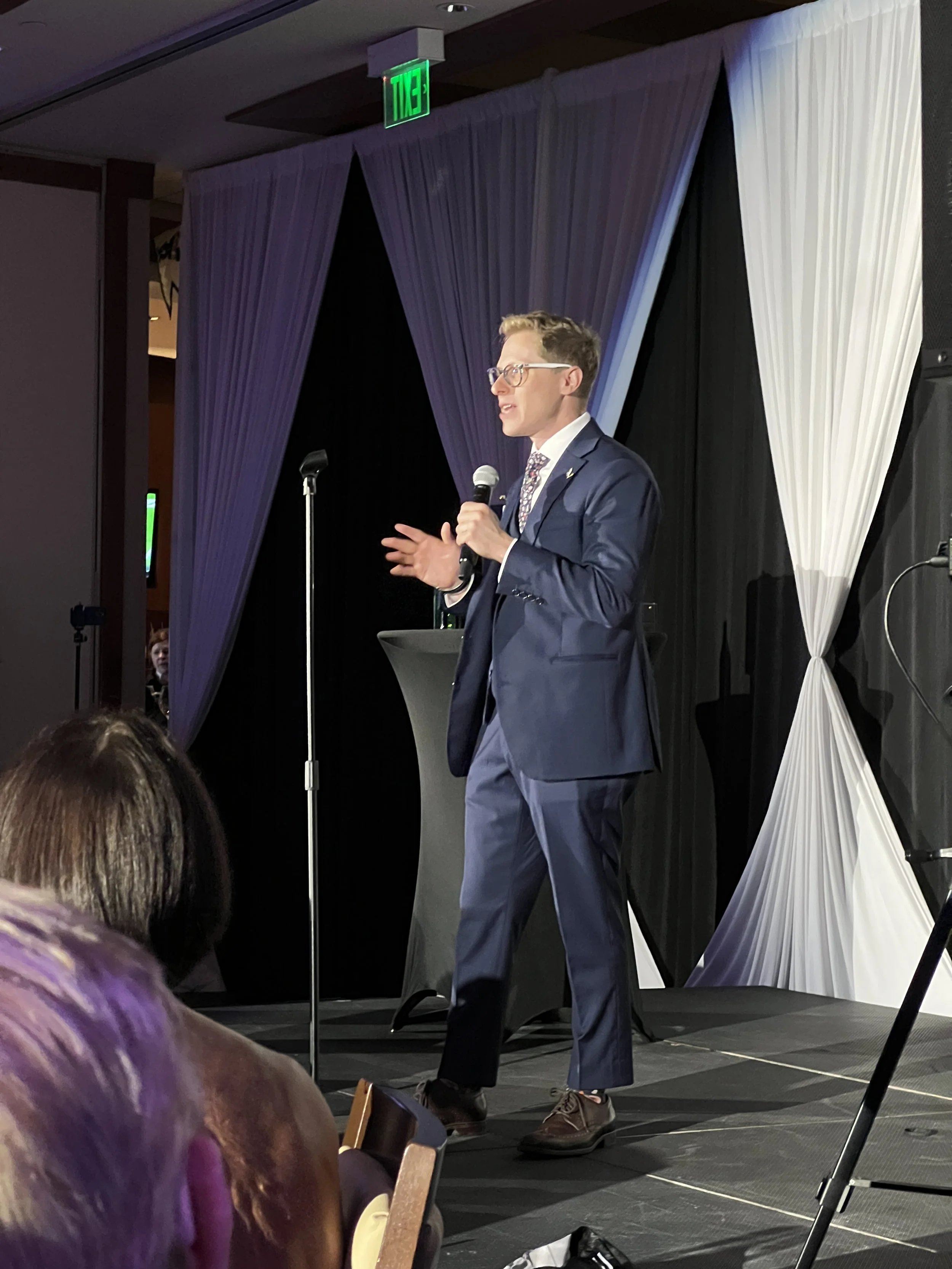 Speaker on stage with draped curtain backdrop at a corporate event in Sarasota
