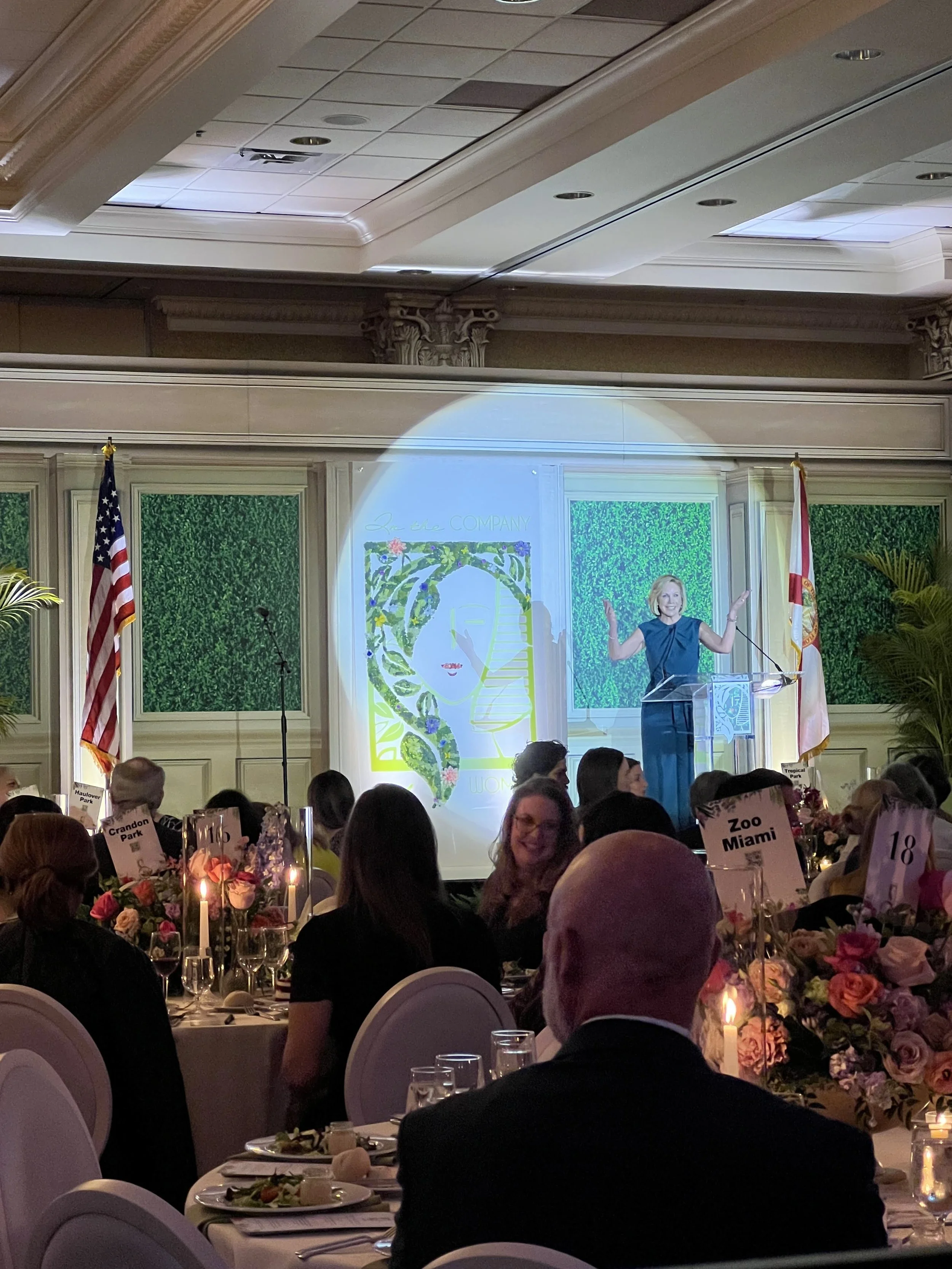 Speaker at podium with green gobo pattern backdrop and seated audience in Sarasota