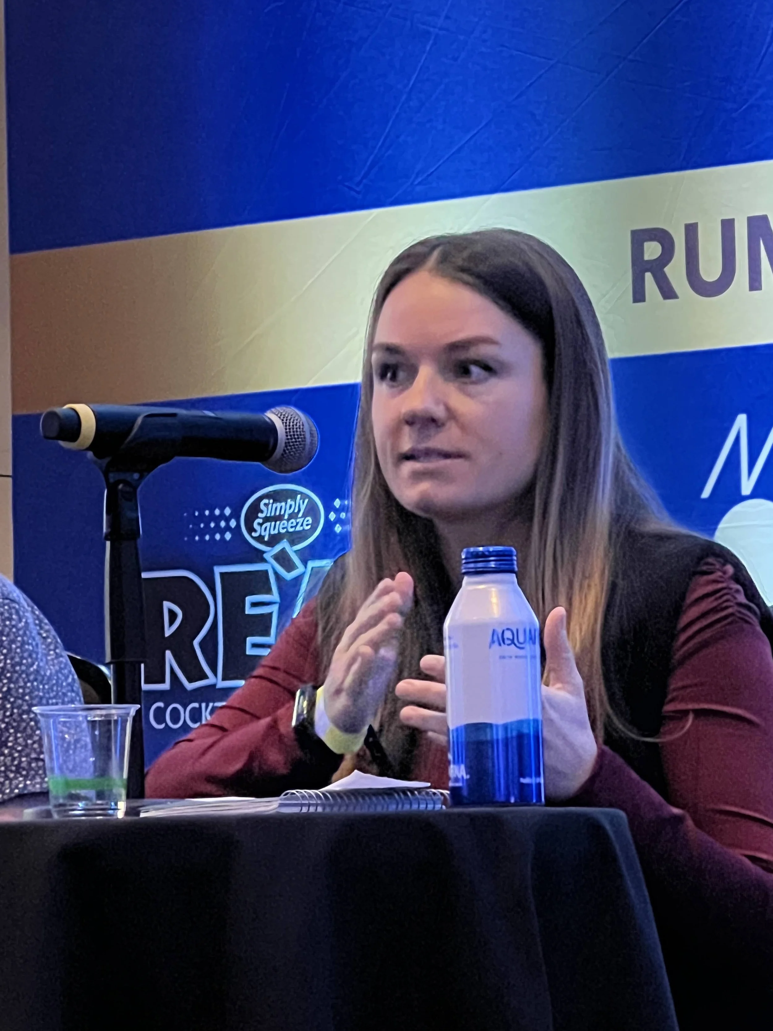 Panelist speaking at a corporate conference with branded signage in Southwest Florida